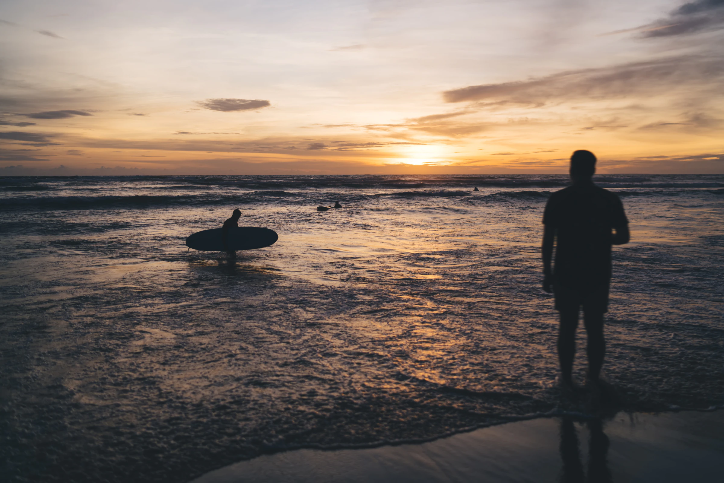 A surfer walking towards the sea across a sandy beach