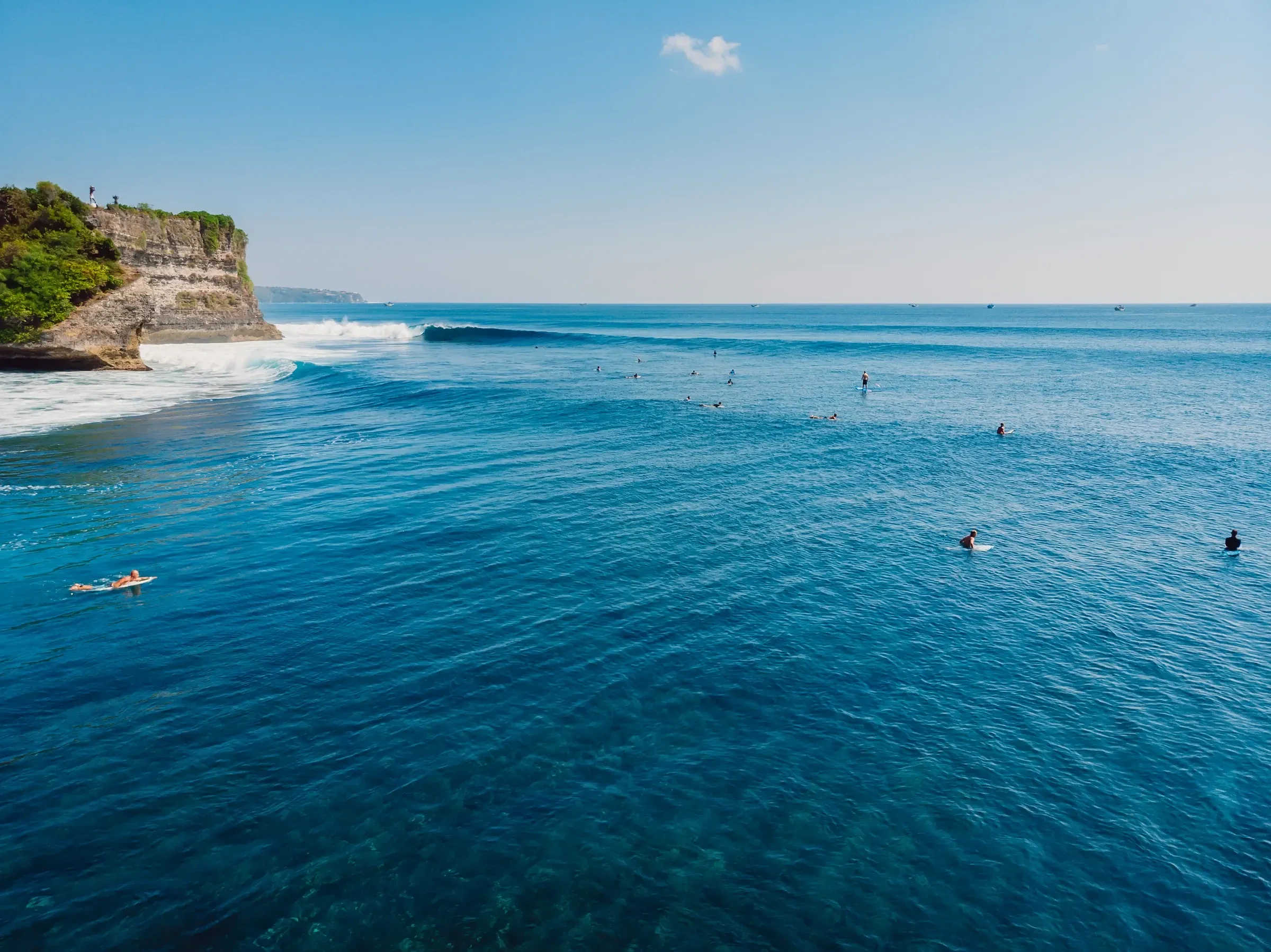 Surfers in the water off a rocky stretch of Bali's coast, seen from above