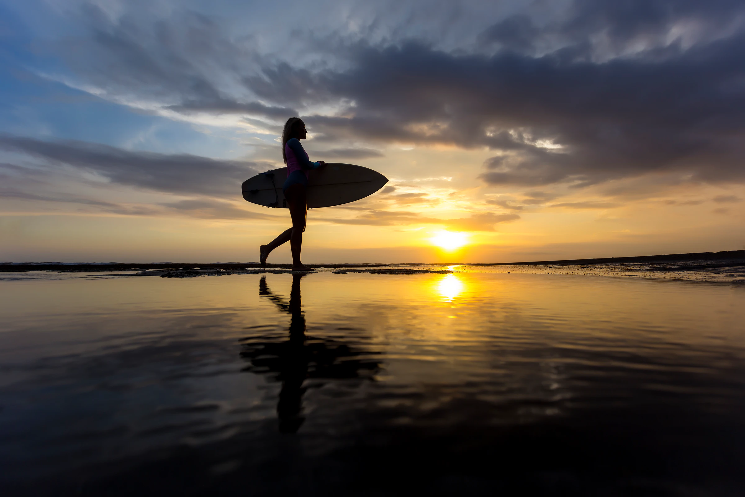 A surfer with a board silhouetted against a Bali sunset