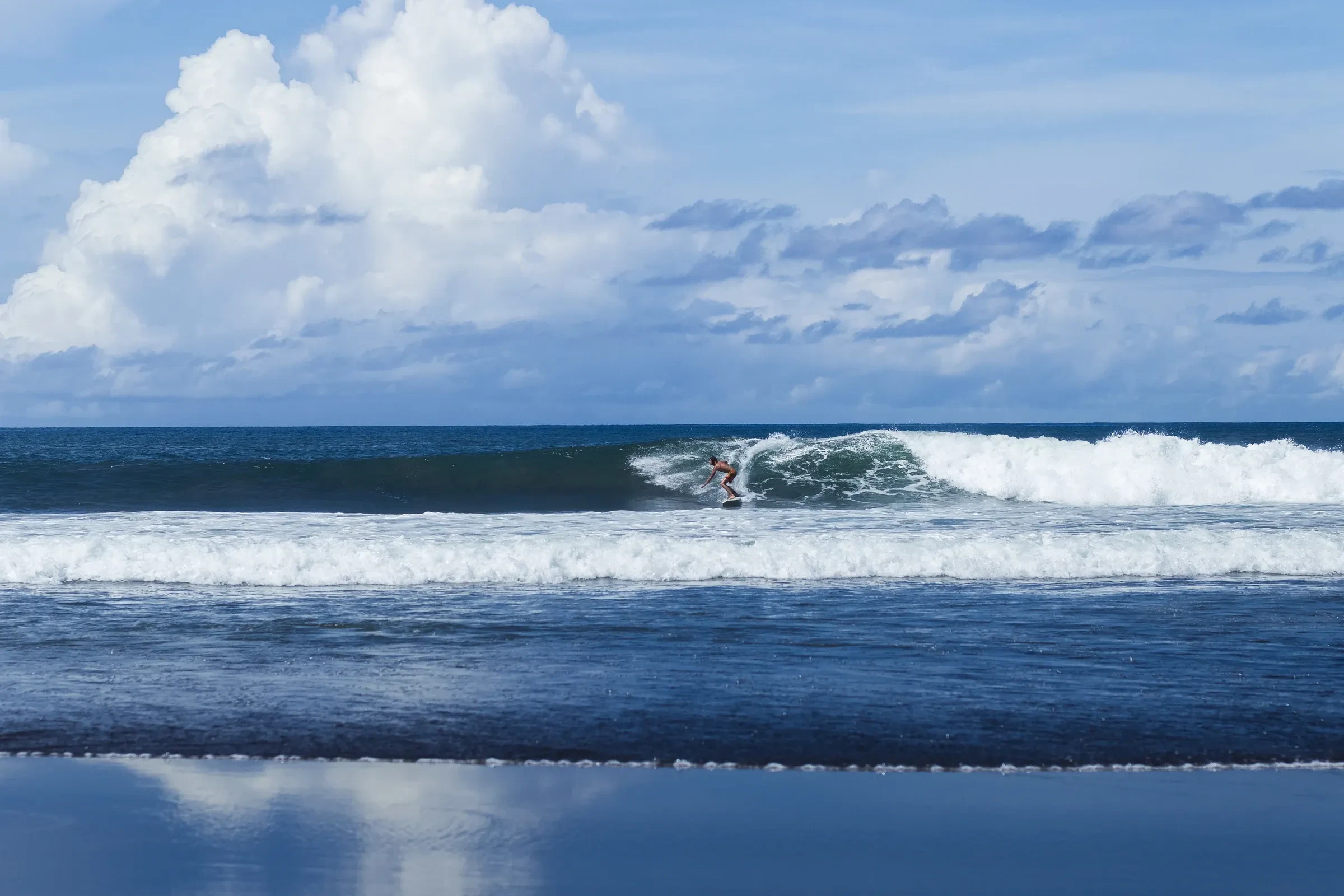 A surfer riding a wave at a Bali surf spot under cloudy skies