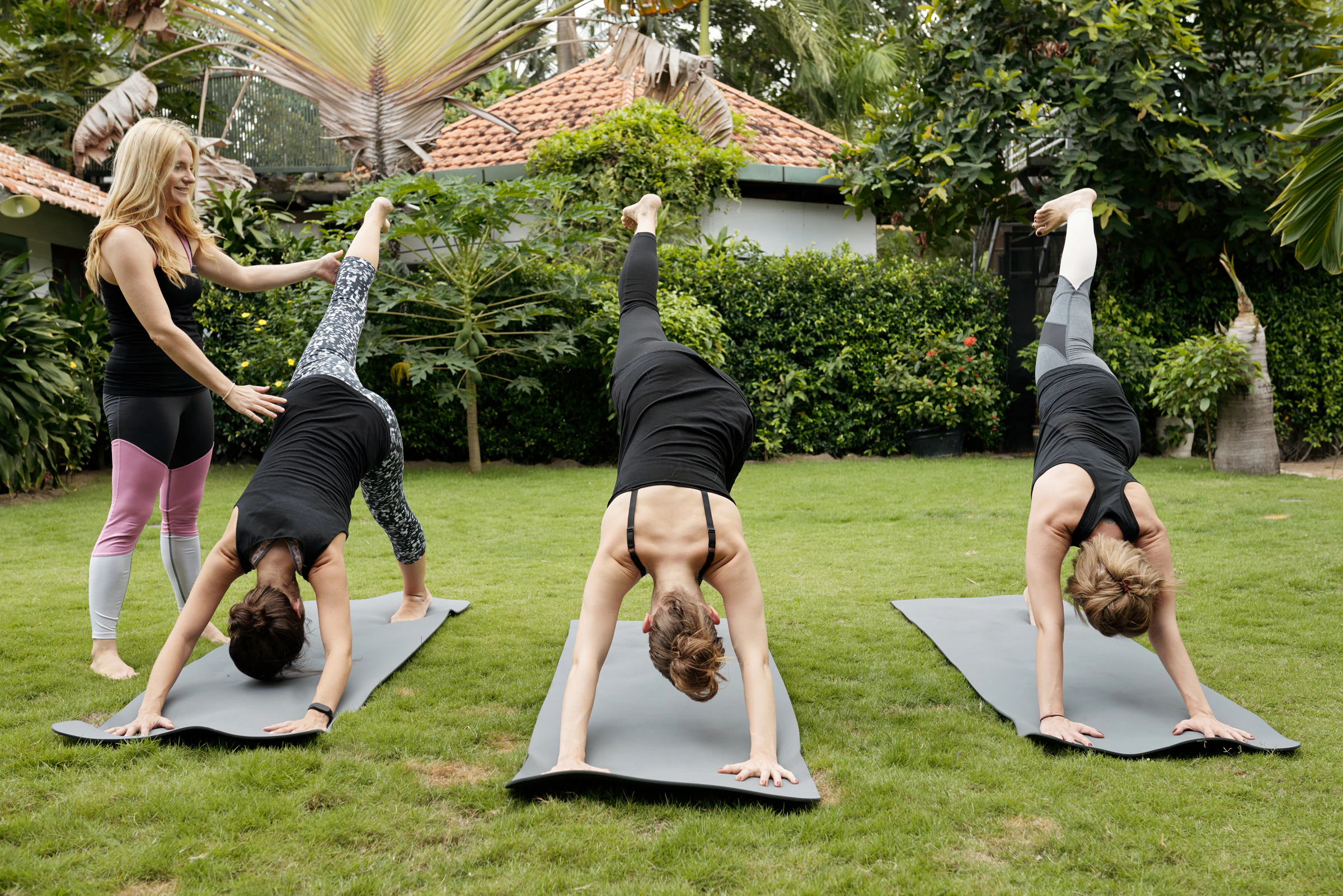 A group practising yoga on mats on a lawn while a teacher adjusts one pose