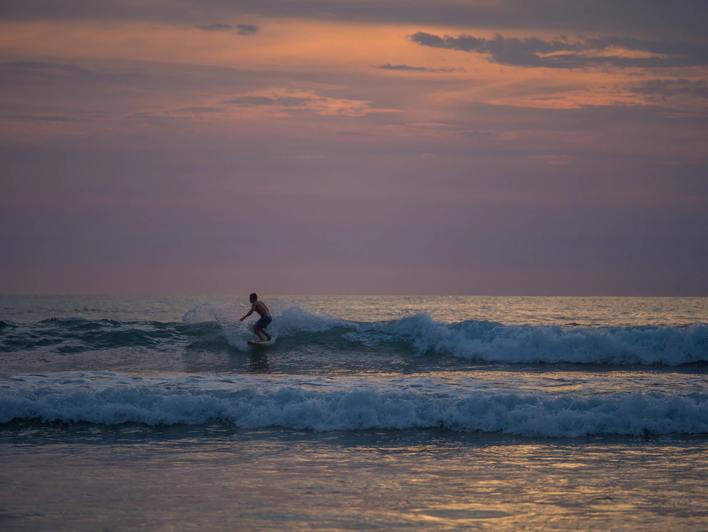 A surfer riding a small wave at dusk