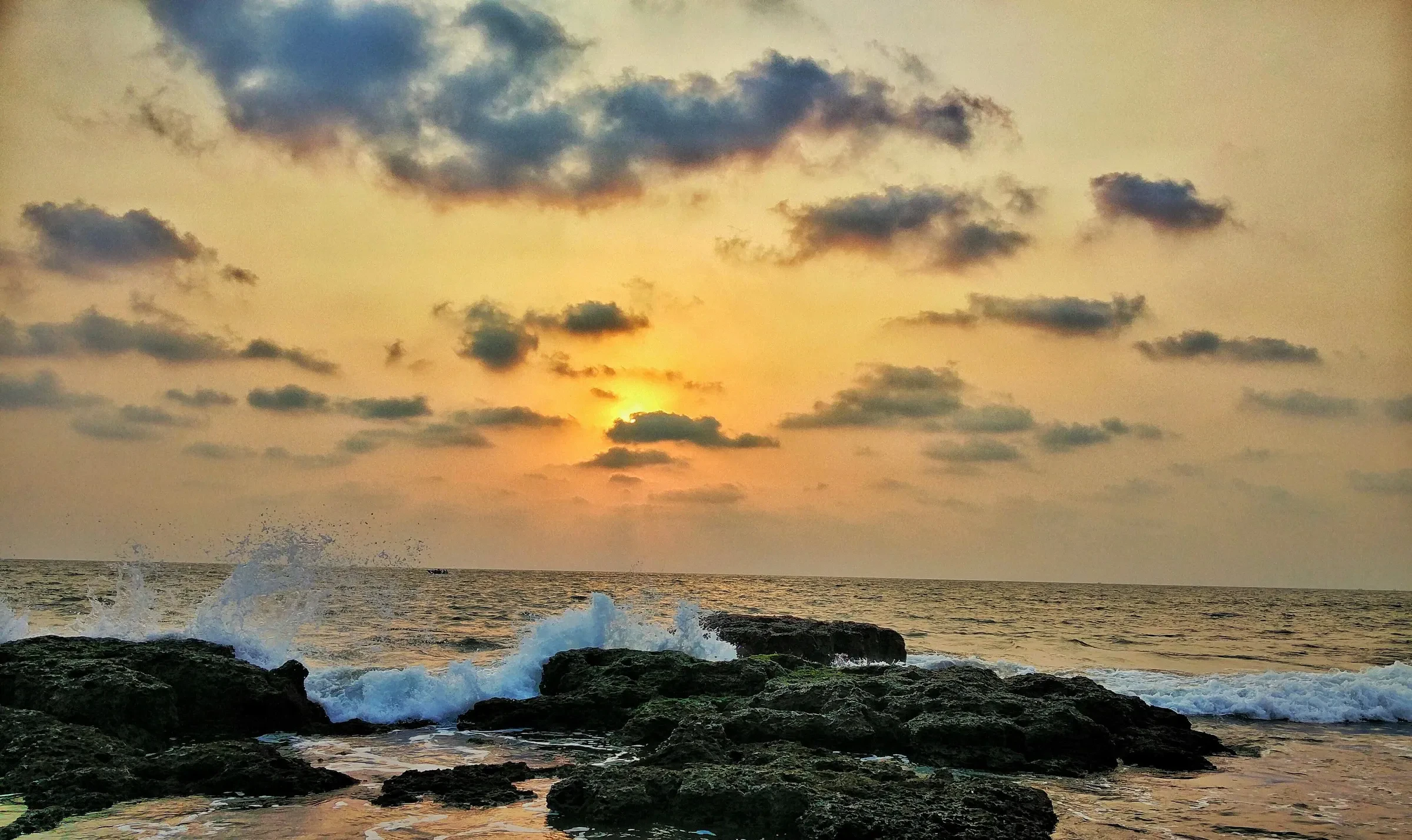 Waves breaking on the dark rocks at Anjuna beach in golden evening light