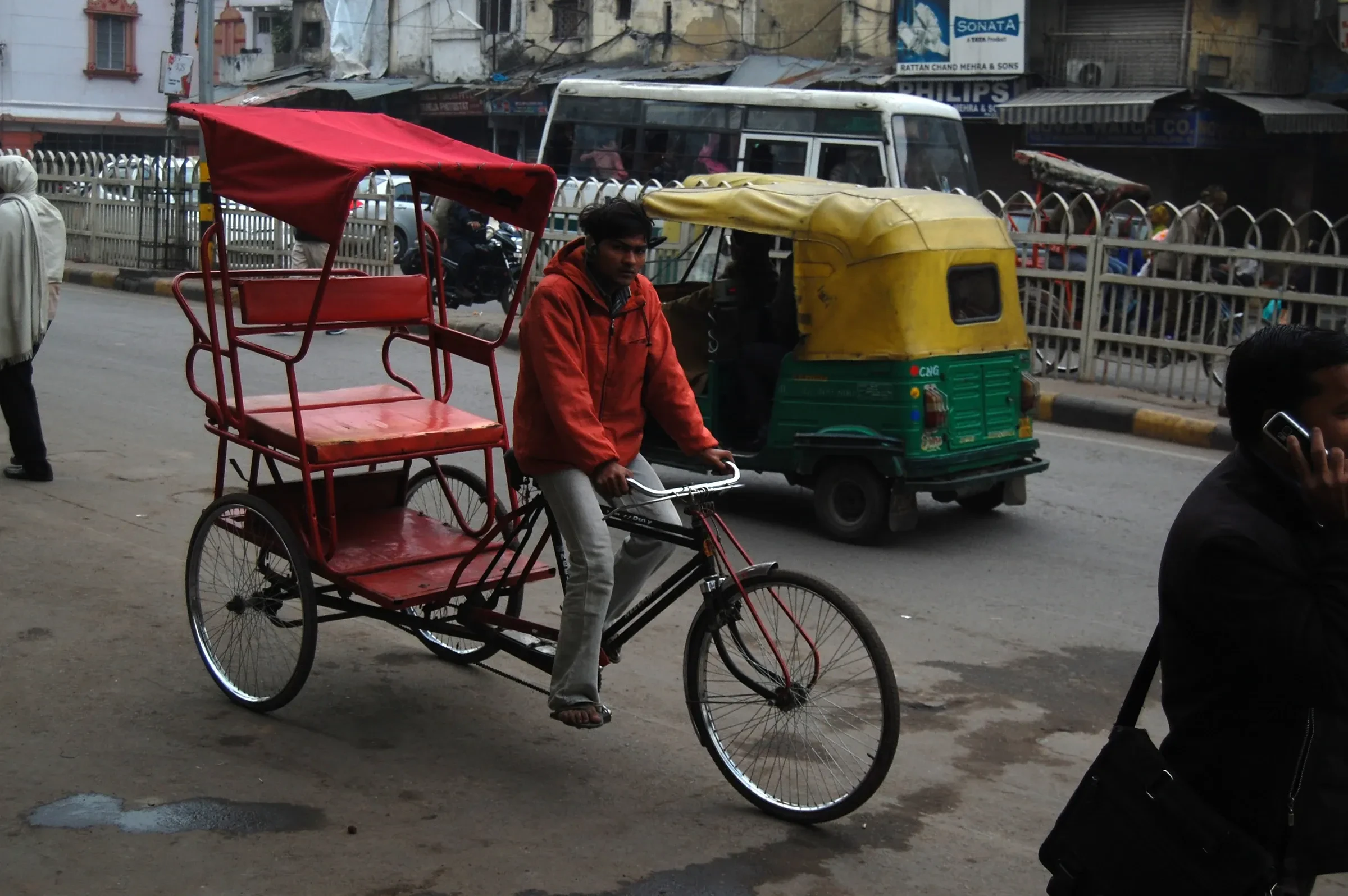 An empty cycle-rickshaw with its rider on a busy Old Delhi street