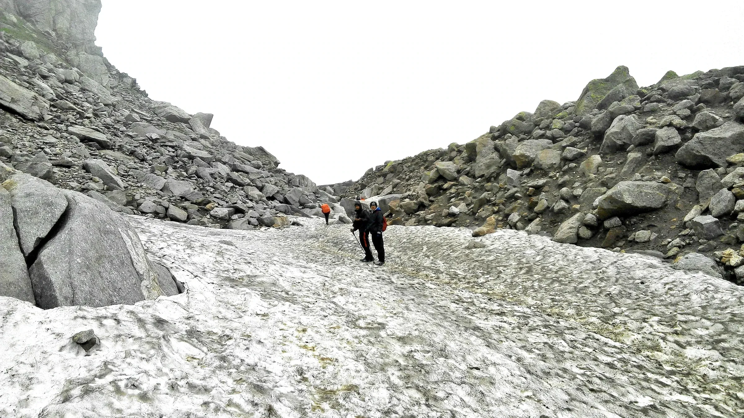 Two trekkers crossing a snowfield between rocky slopes near Hampta Pass