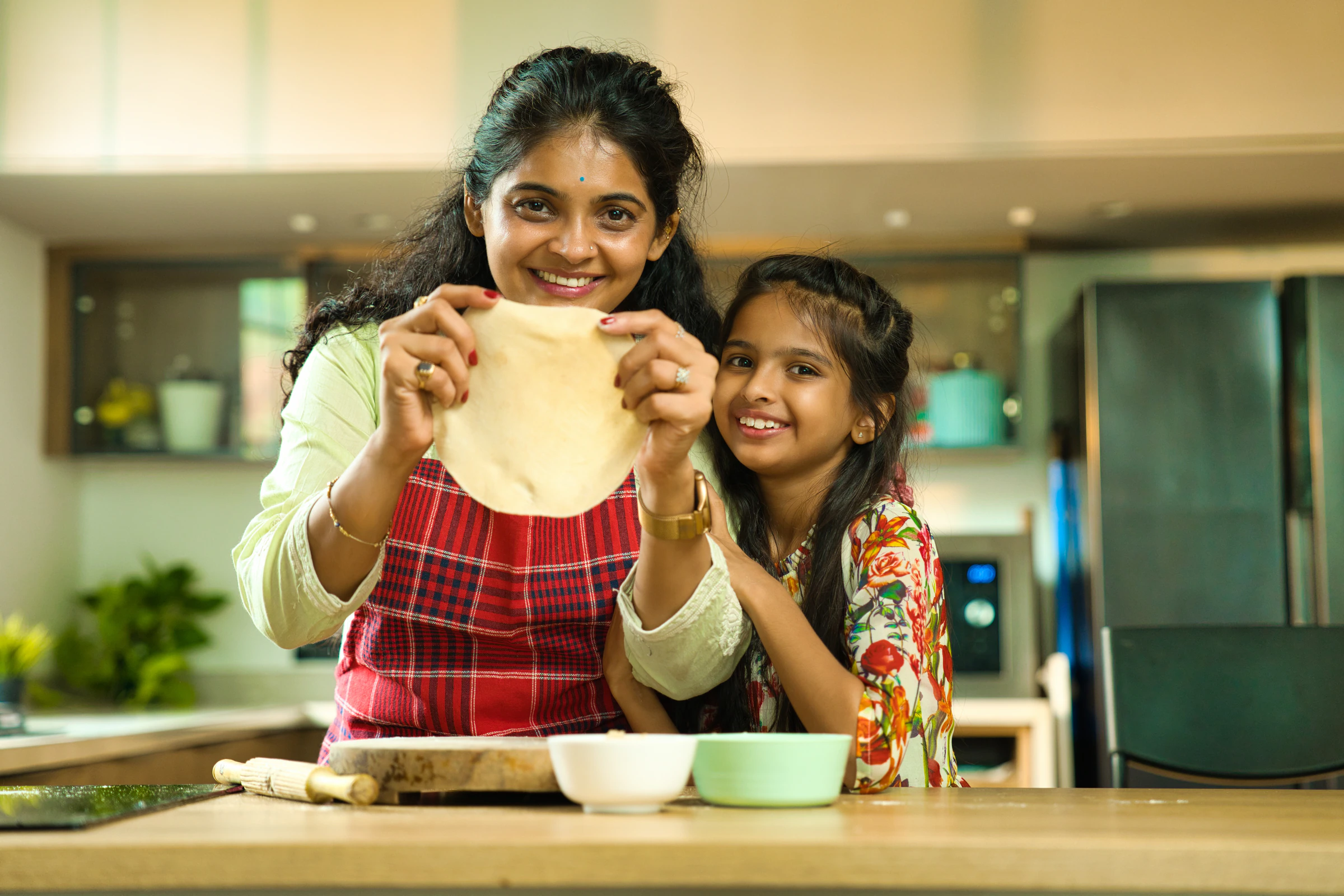 A mother and daughter rolling chapati dough in a home kitchen