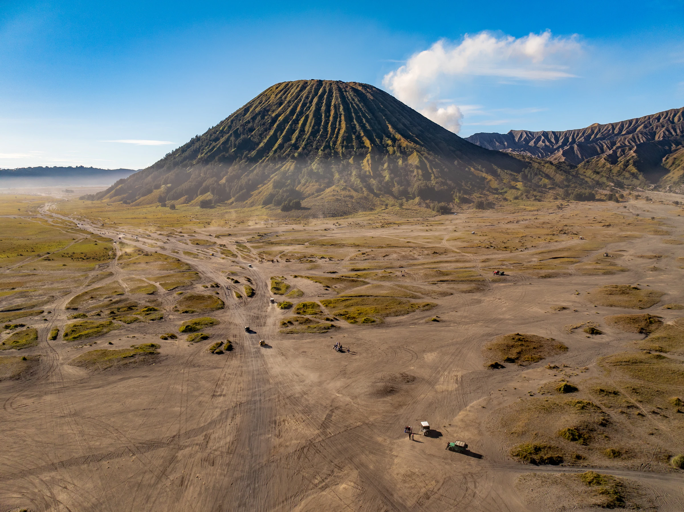 Mount Bromo rising from the sea of sand, with jeeps on the track below