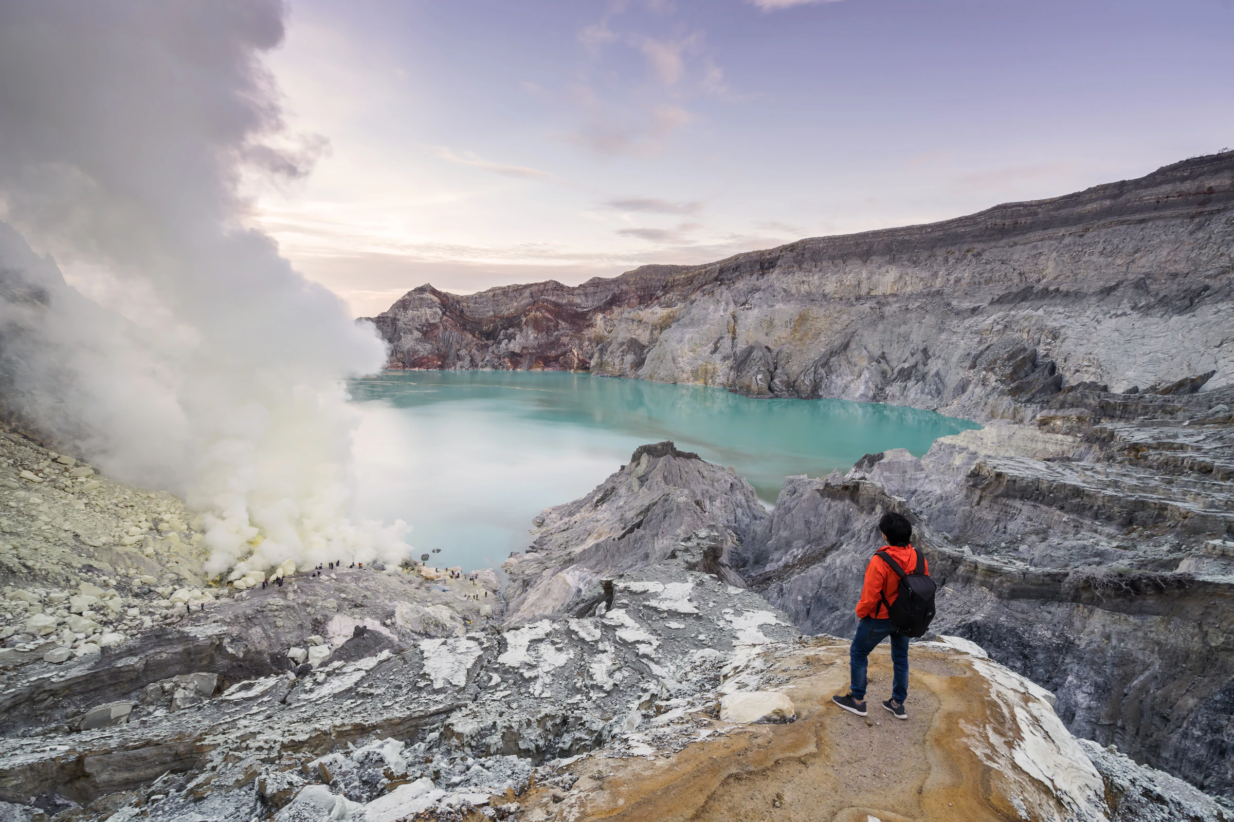 A hiker on the rim of the Ijen crater above the turquoise lake
