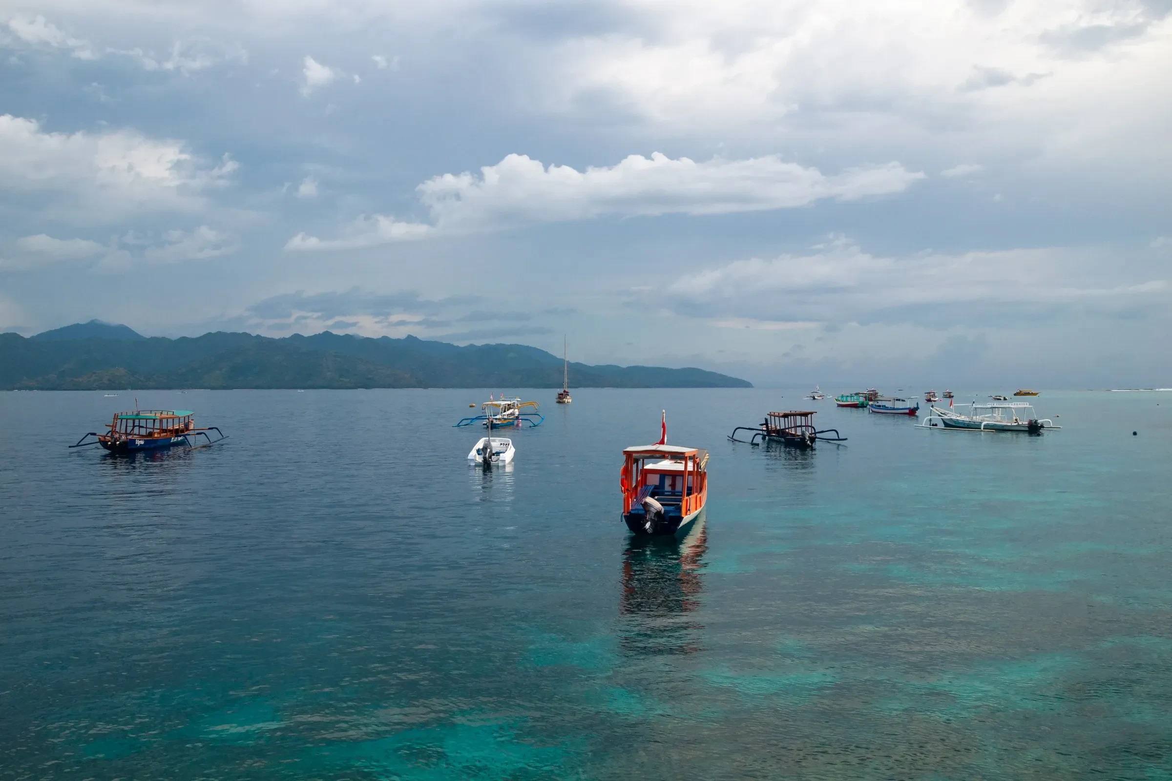 Small wooden boats anchored over a shallow reef in the Gili Islands