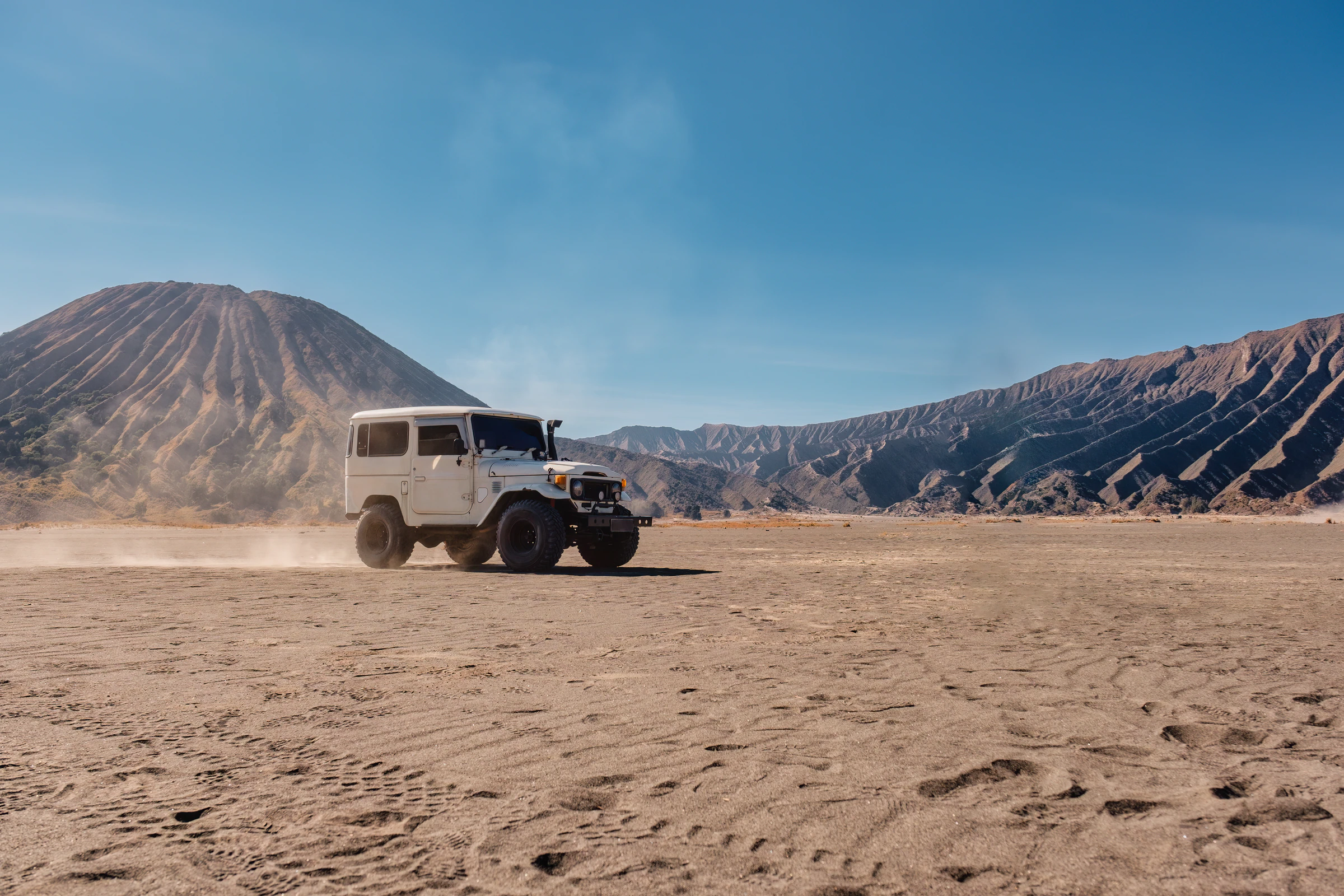 An off-road jeep on the volcanic sand below Mount Bromo