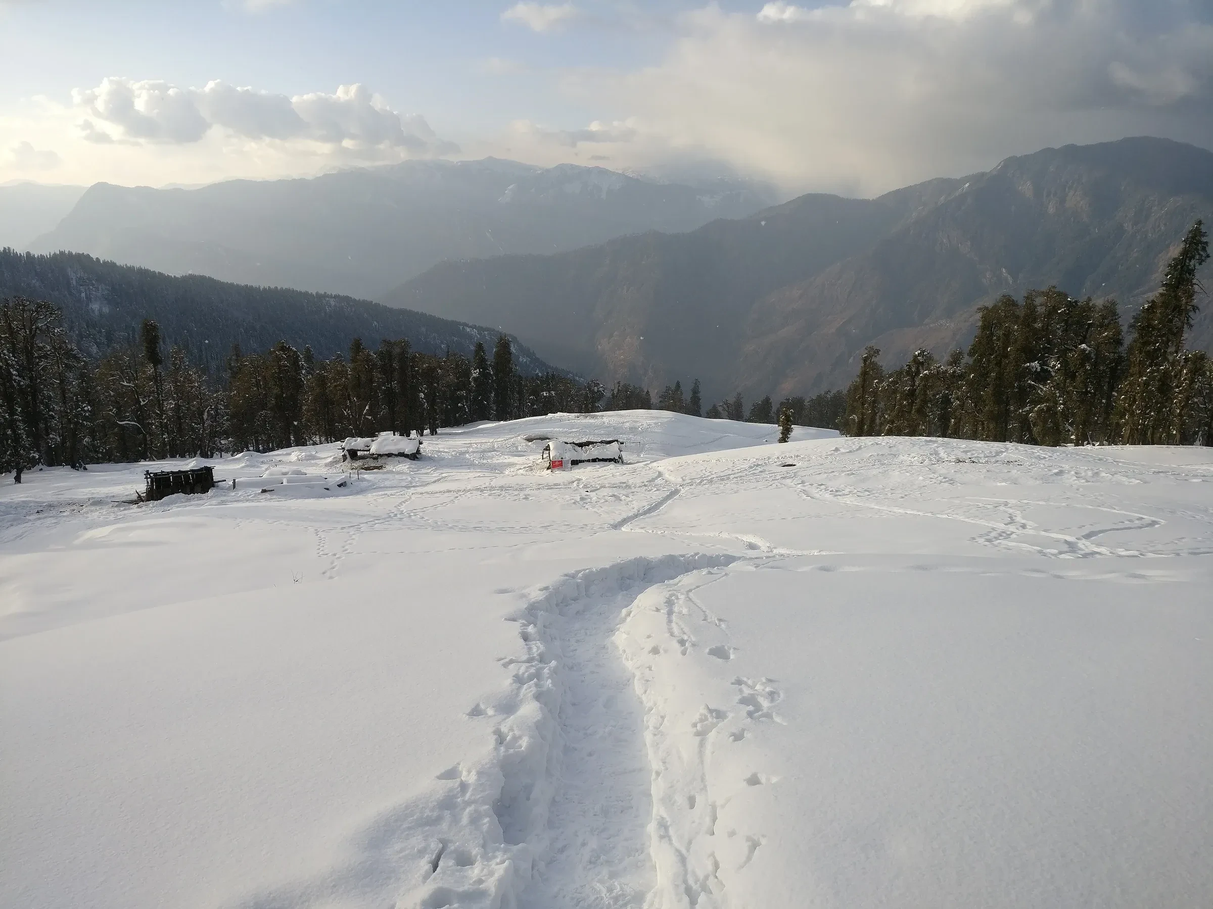 A trodden path across an open snow meadow on the way to Kedarkantha