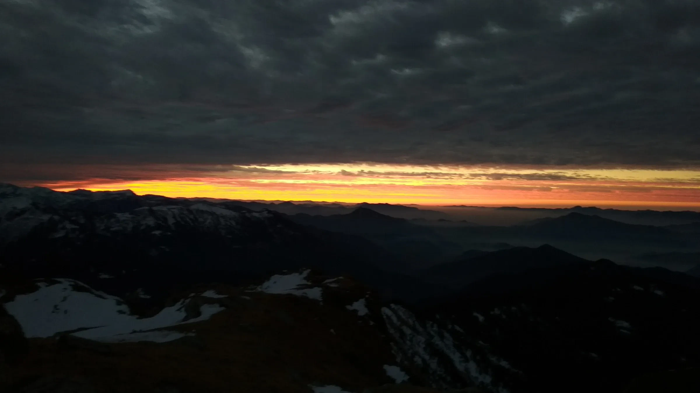 First light on the horizon at the Kedarkantha summit with dark ridges below