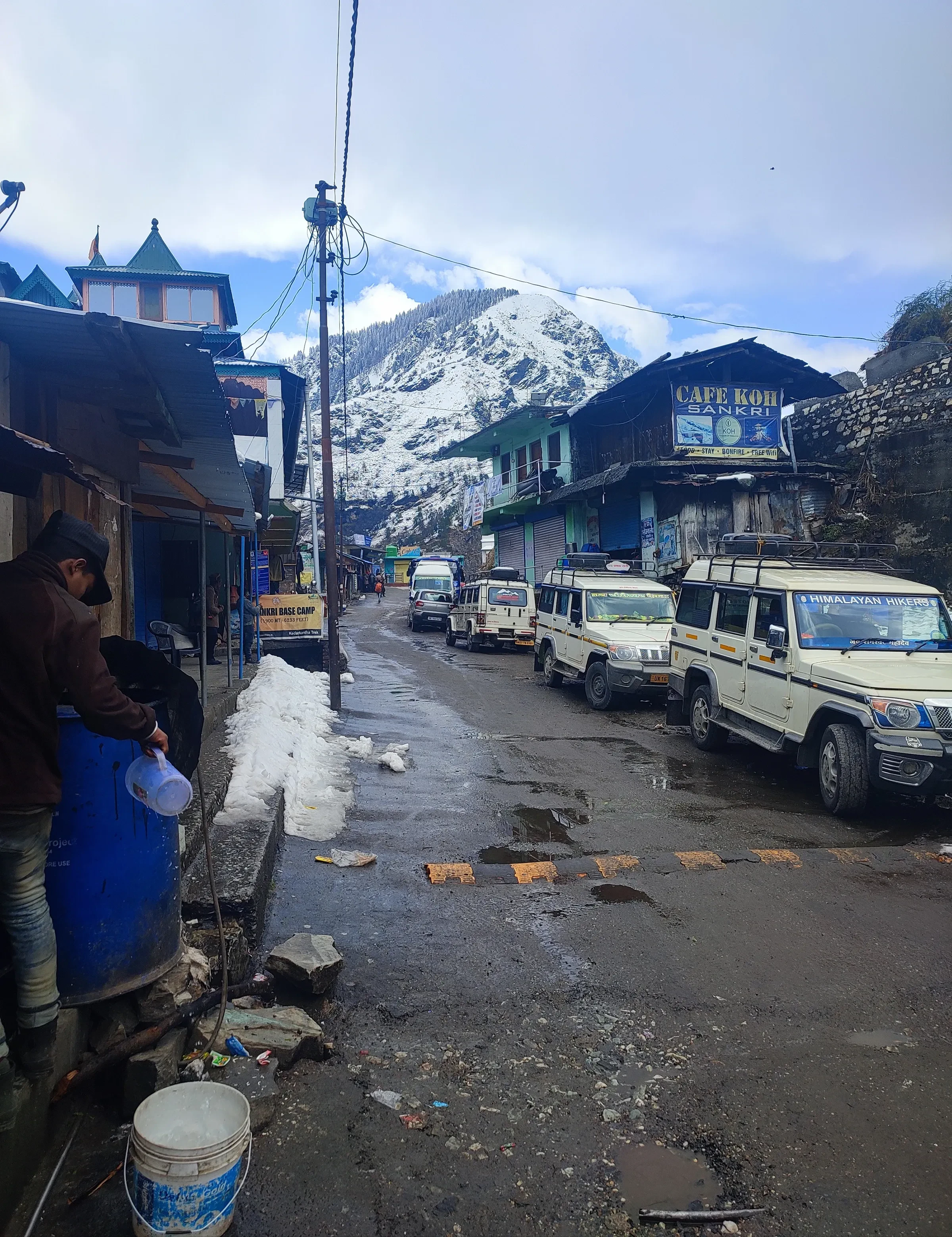 A street in Sankri with parked jeeps, shopfronts and a snow peak behind