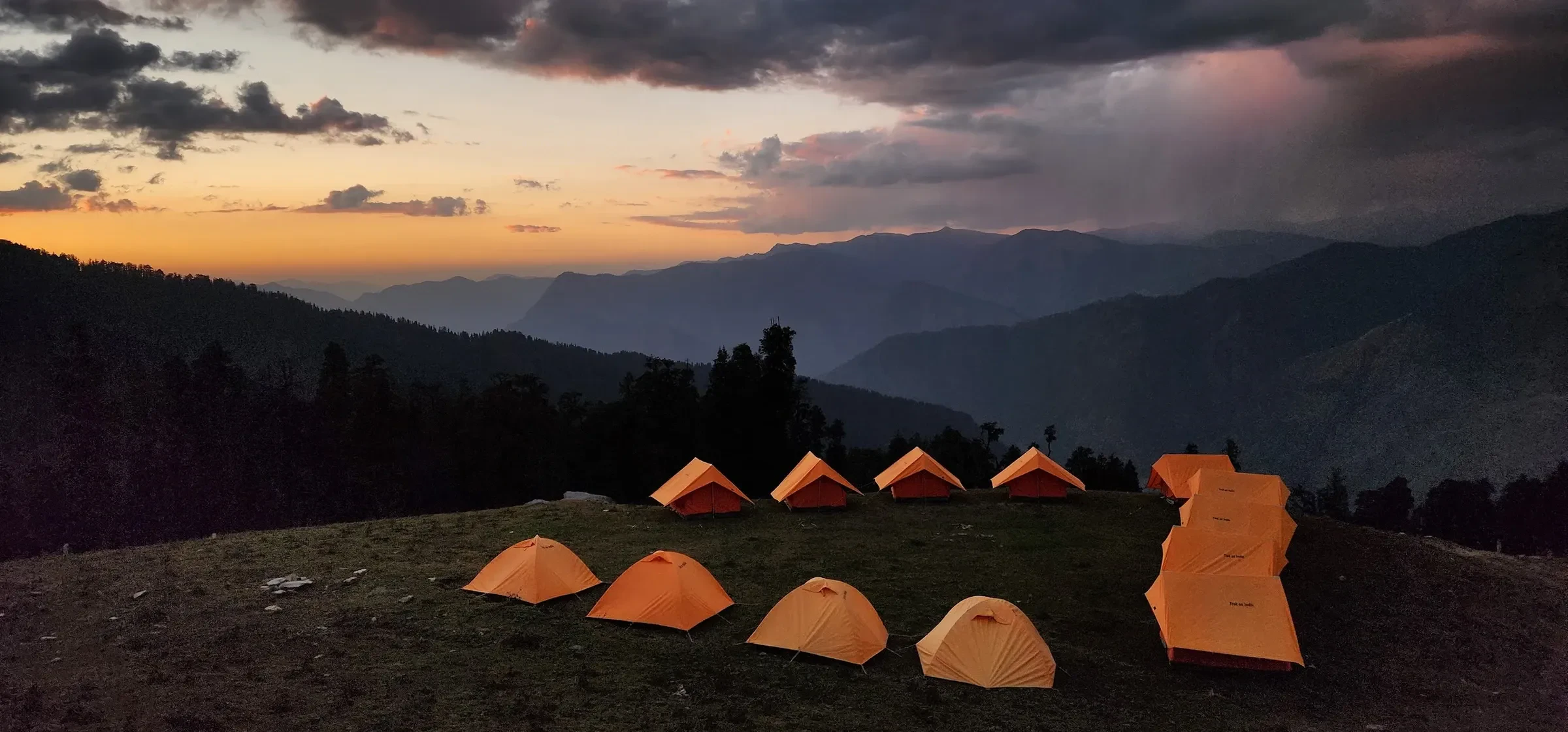 Orange trekking tents pitched on a meadow below the mountains at dusk