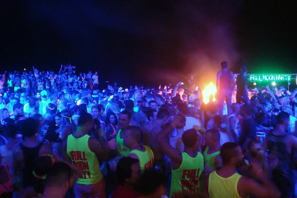 A crowd dancing on Haad Rin beach at a Full Moon Party, lit in blue and green
