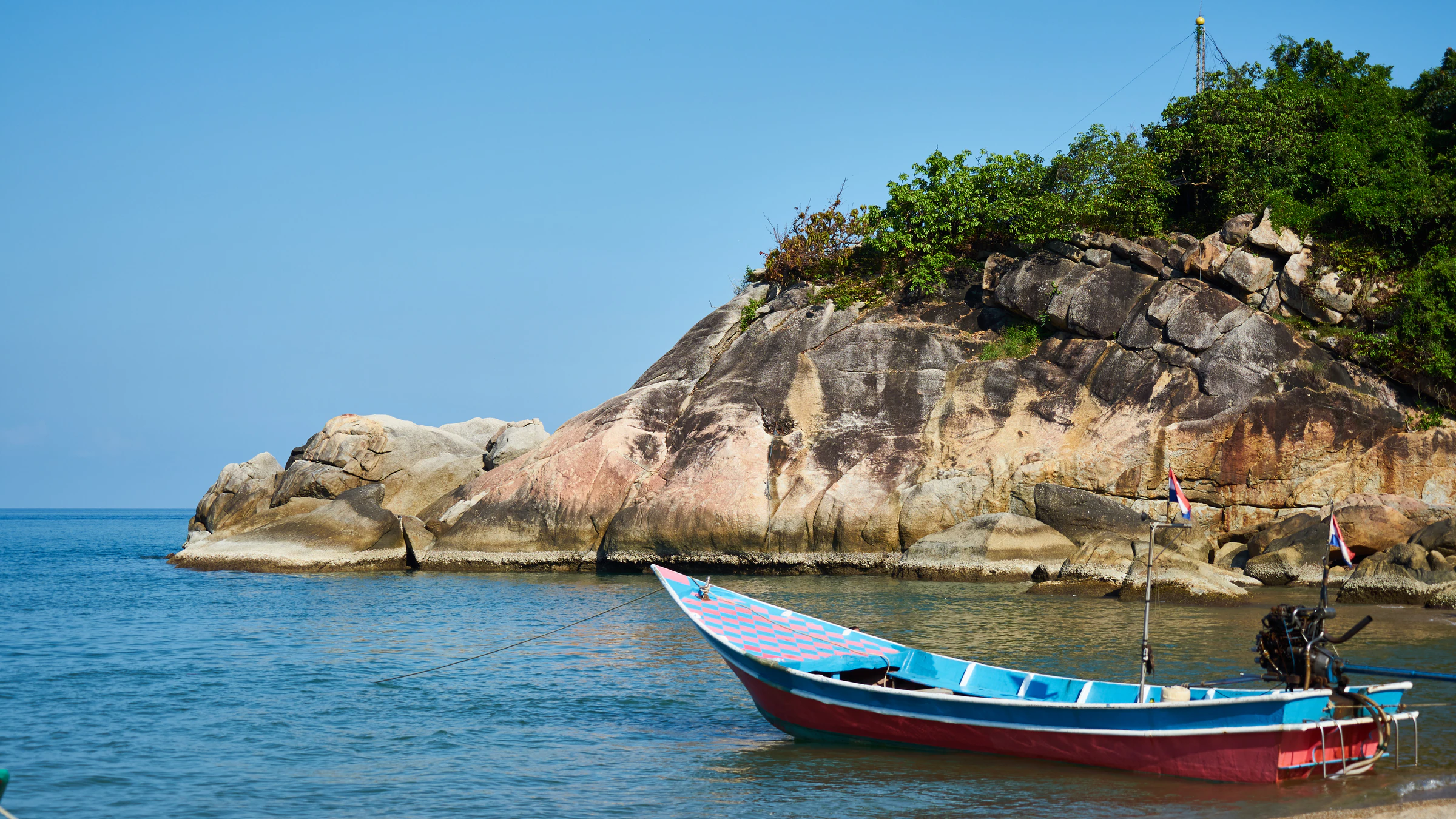 A small fishing boat anchored beside a granite headland on Koh Phangan