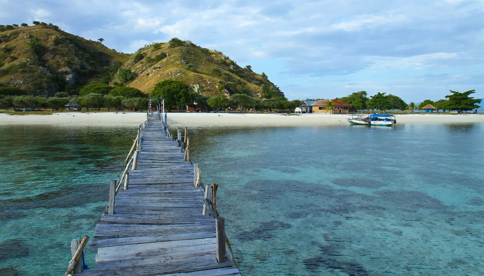 A wooden jetty running over clear shallow water to the beach on Kanawa Island