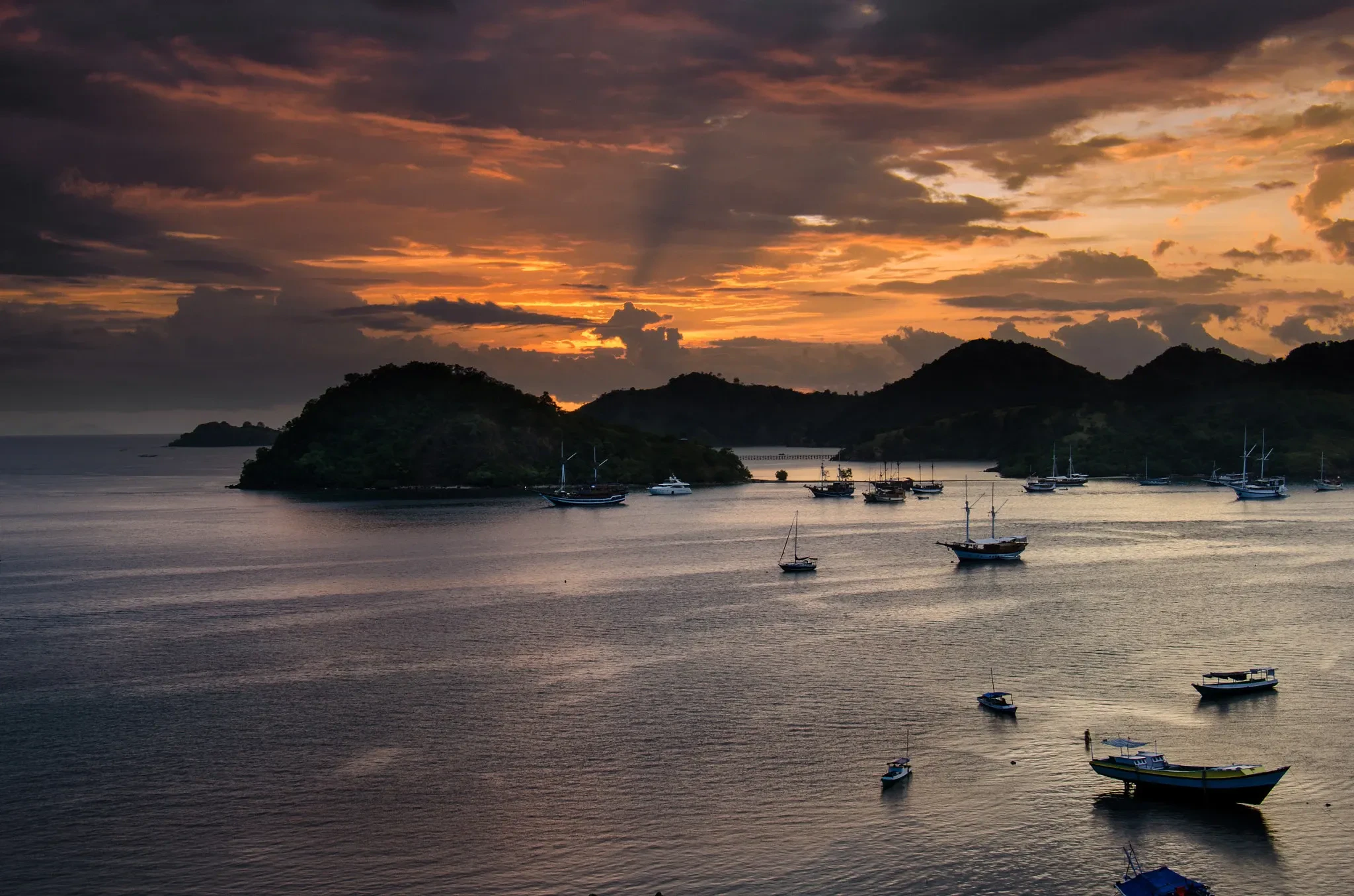 Fishing boats in the bay at Labuan Bajo under an orange sunset sky