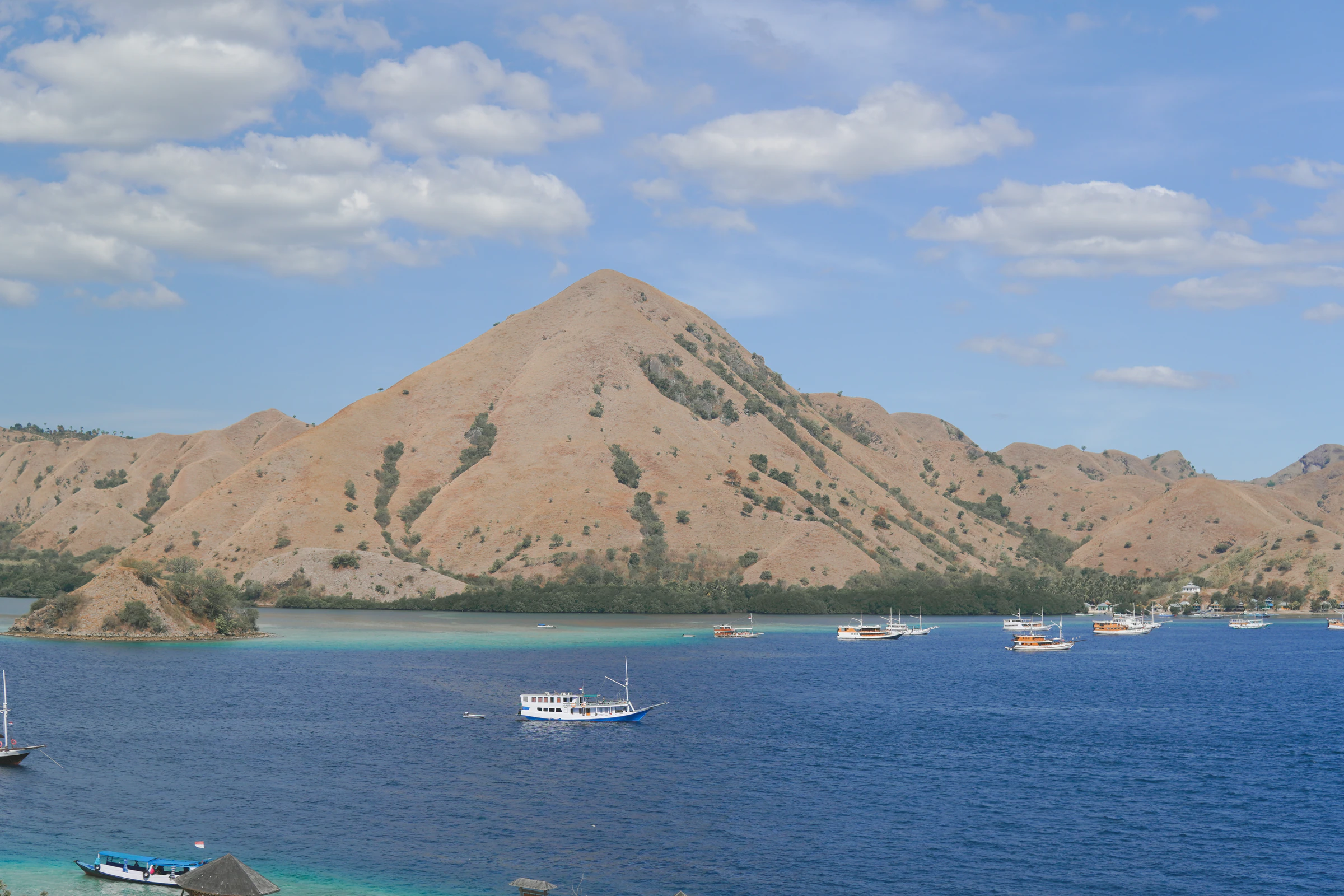 A dry hill rising from the water with boats at anchor near Labuan Bajo
