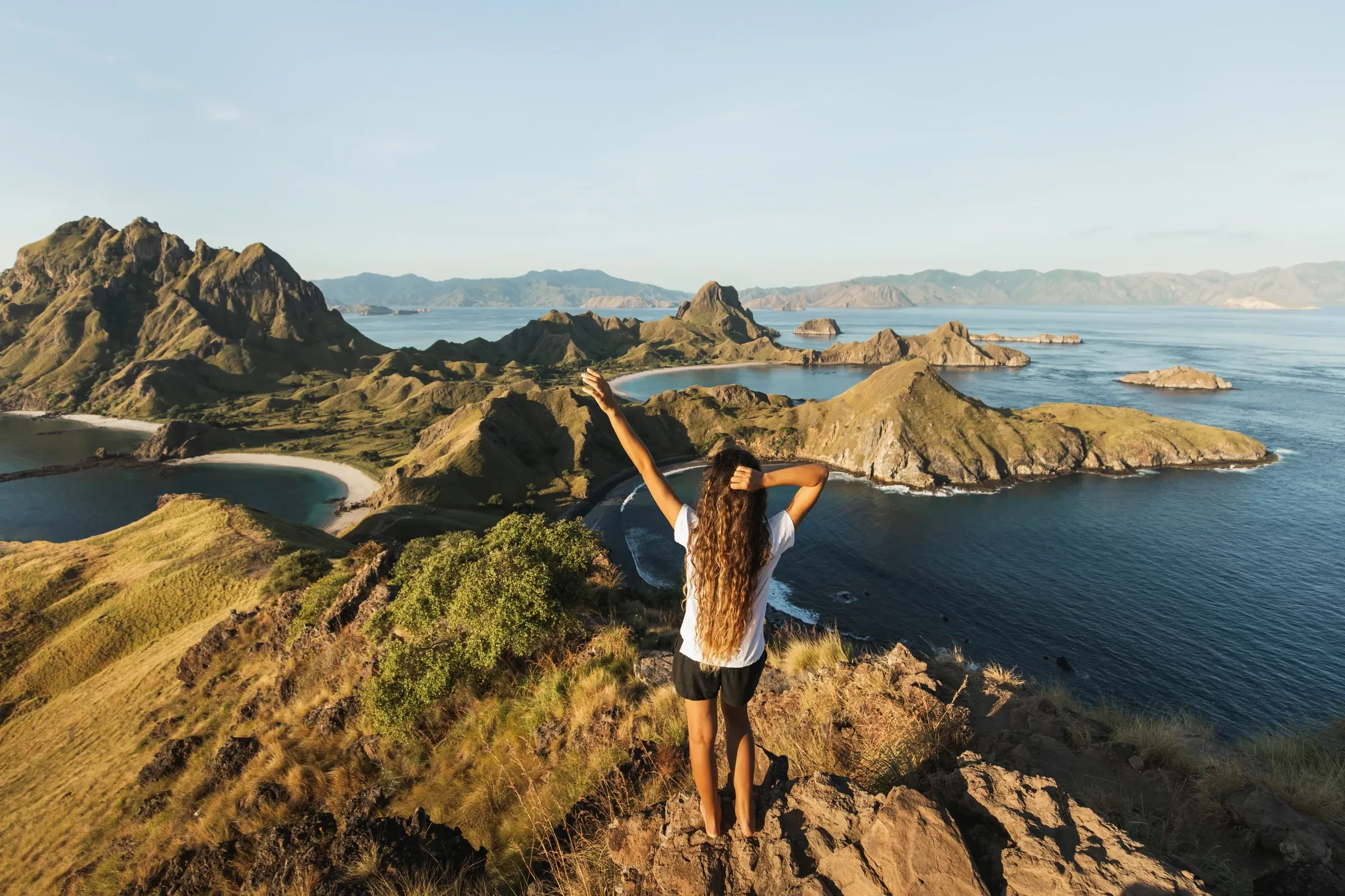 A traveller with arms raised on the Padar ridge above the island's curved bays