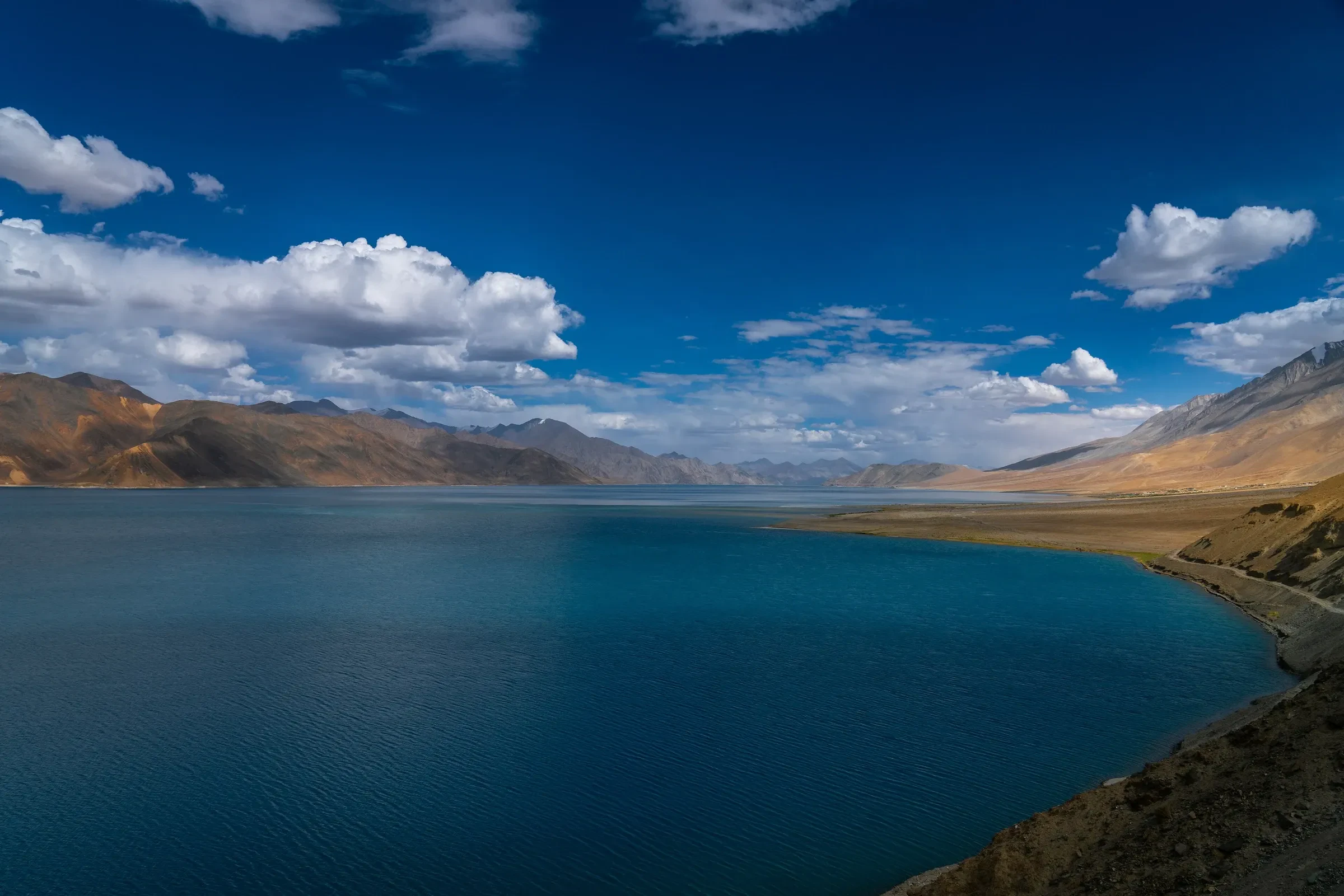 Deep blue water of Pangong Lake below brown mountains and bright clouds
