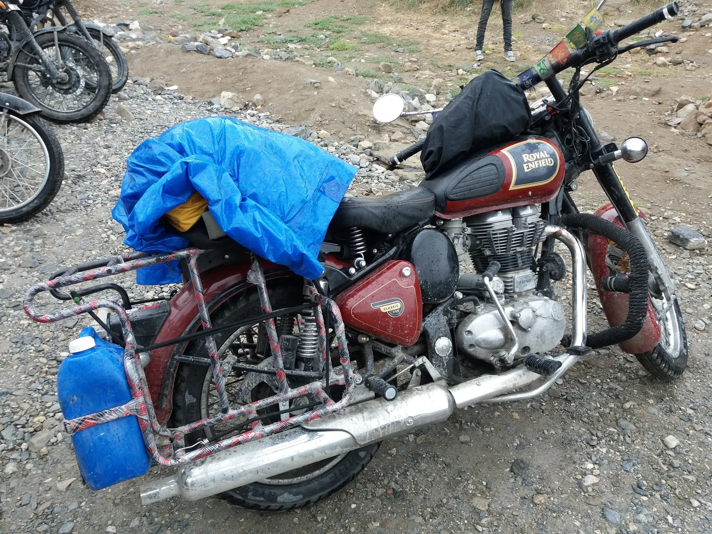 A Royal Enfield Bullet loaded with jerry cans and a tarpaulin, parked on gravel beside the Leh-Manali highway