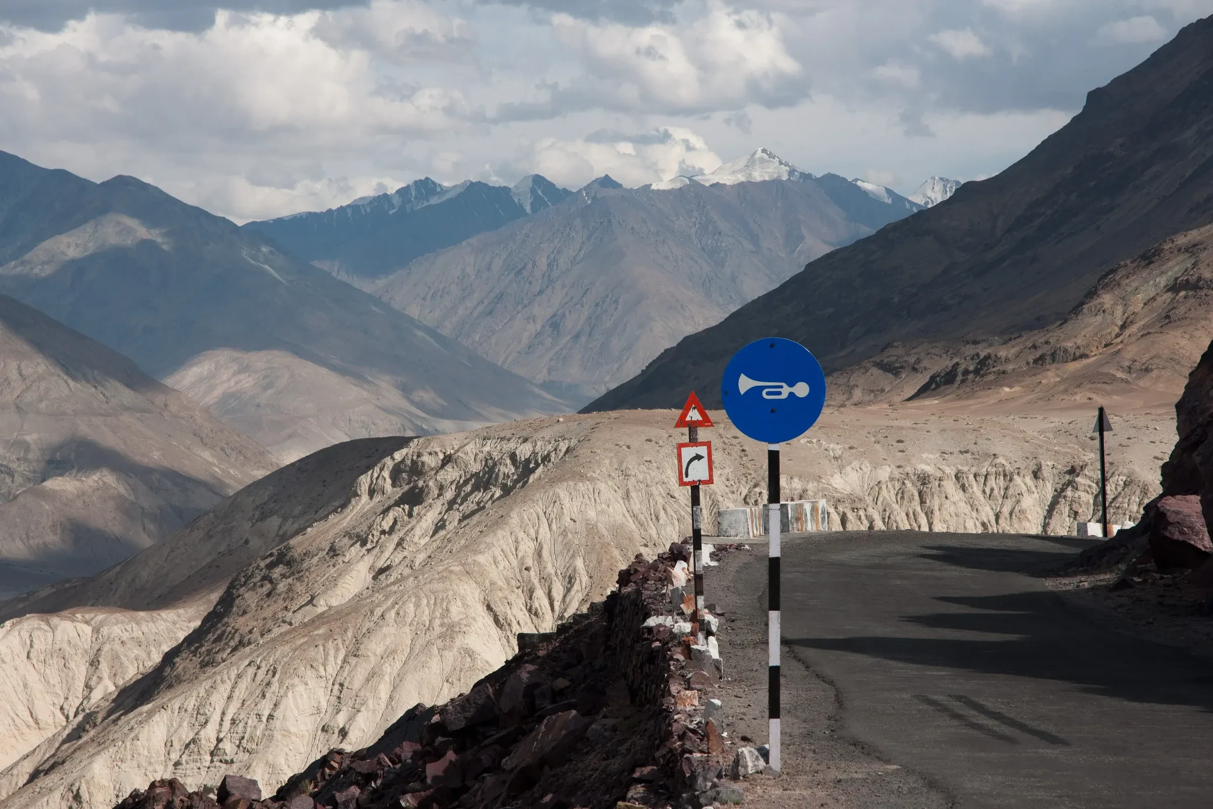 A tarmac bend with road signs high on the Khardung La road above a Himalayan valley