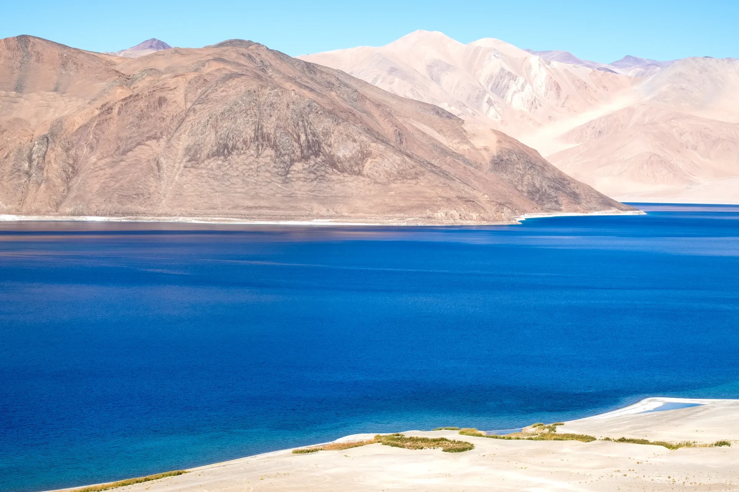 Deep blue Pangong Lake with a pale shoreline and mountains behind in Ladakh