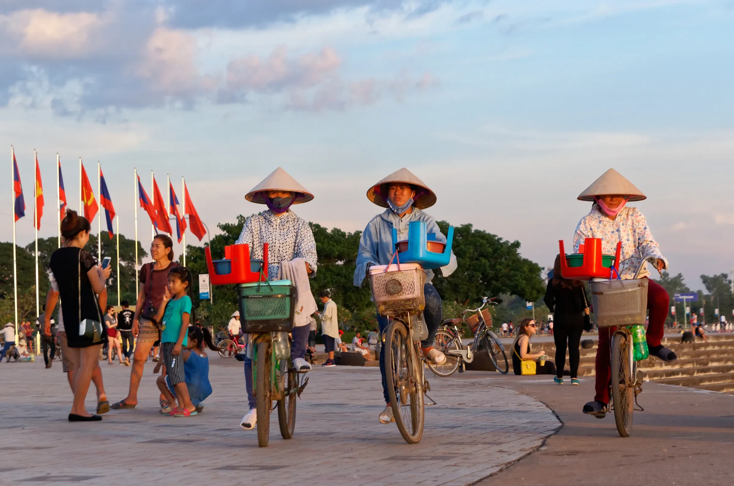Cyclists in conical hats and families on the Mekong riverfront in Vientiane at sunset