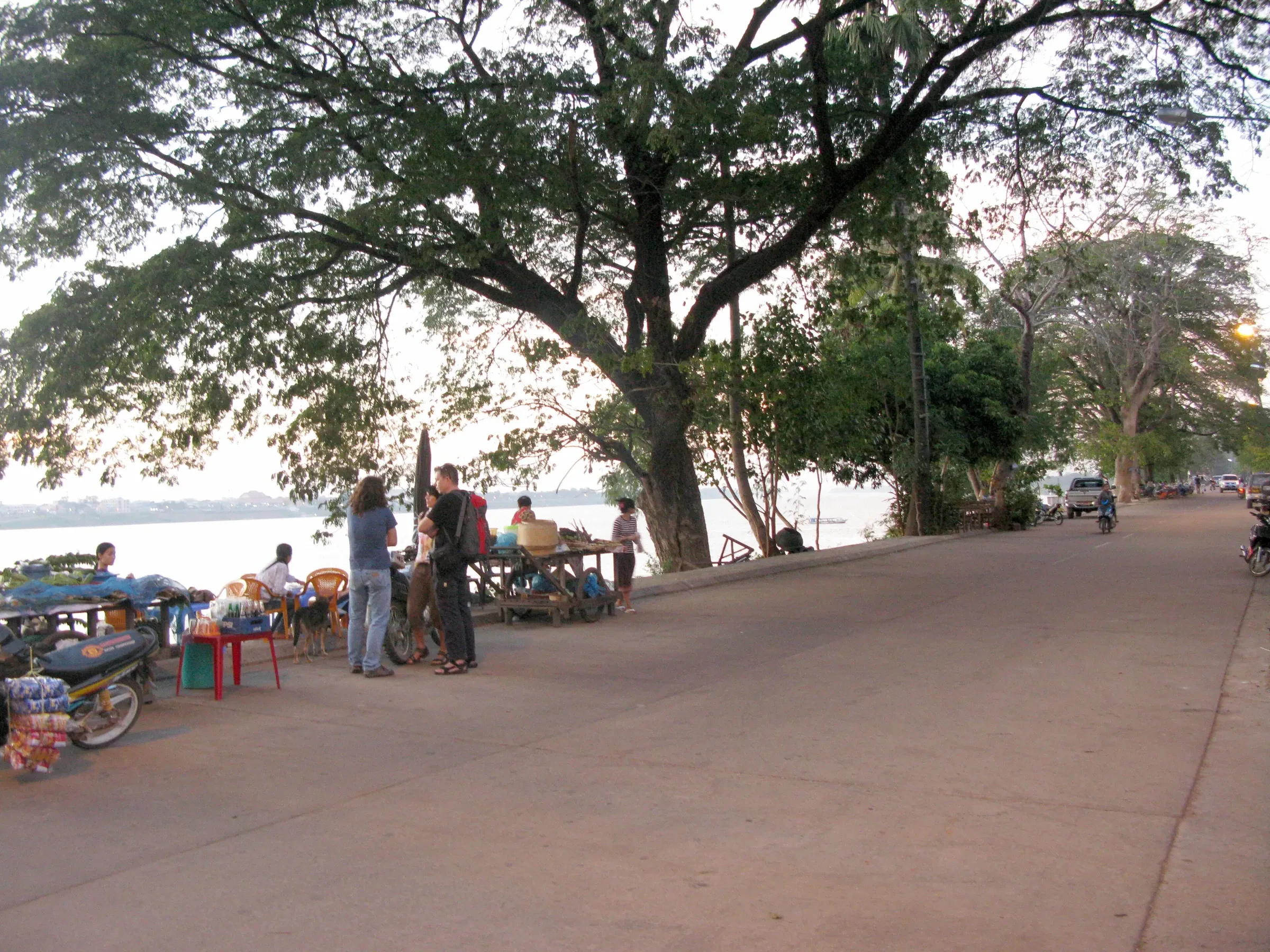 A riverside road lined with trees and people on the Mekong bank in Thakhek