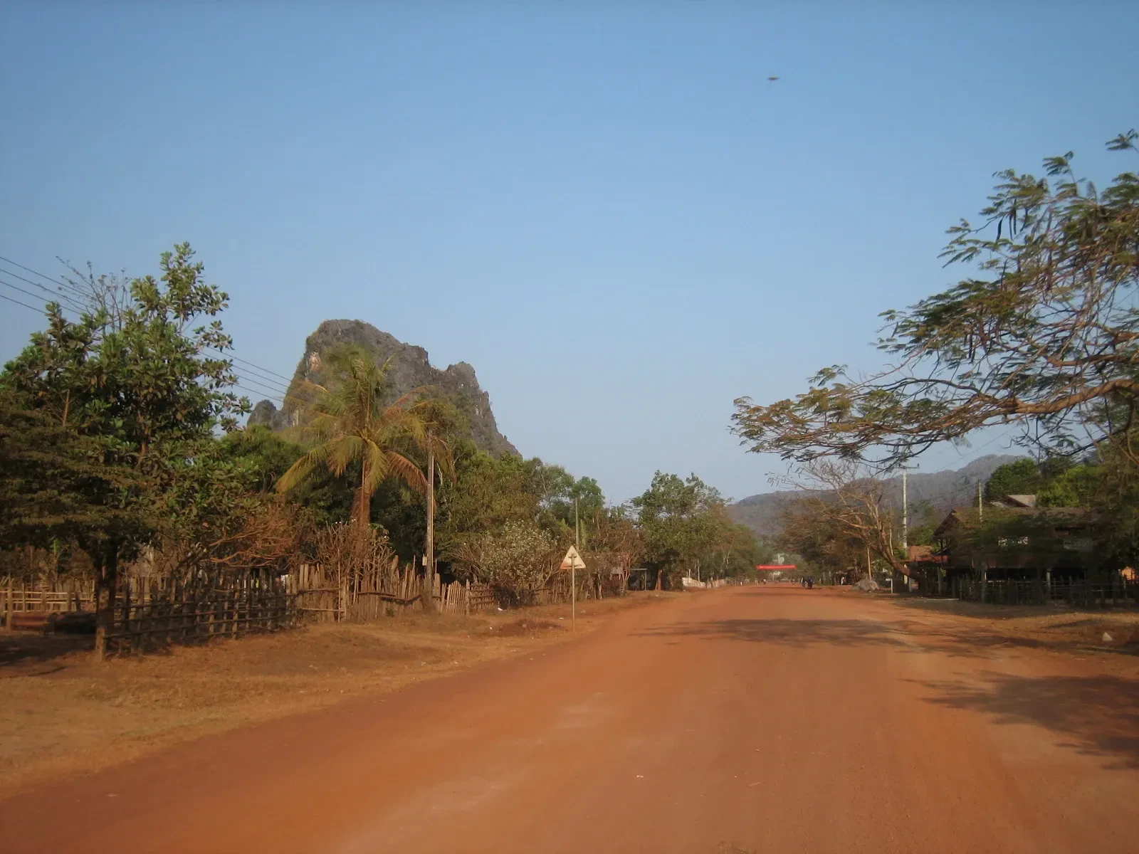 A red dirt road through a village below limestone hills in Khammouane Province