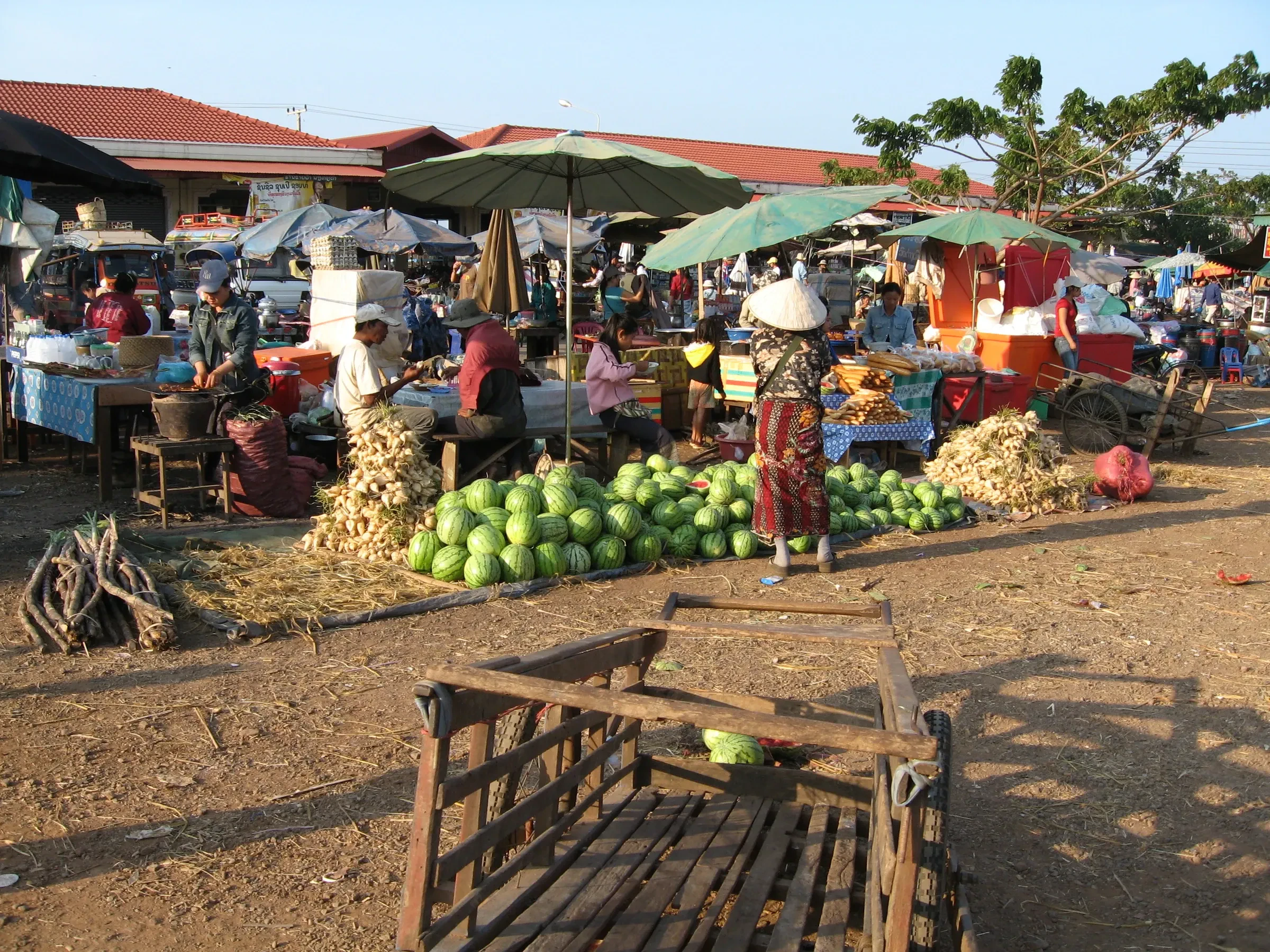 A busy outdoor market with melons and sunshades in Pakse