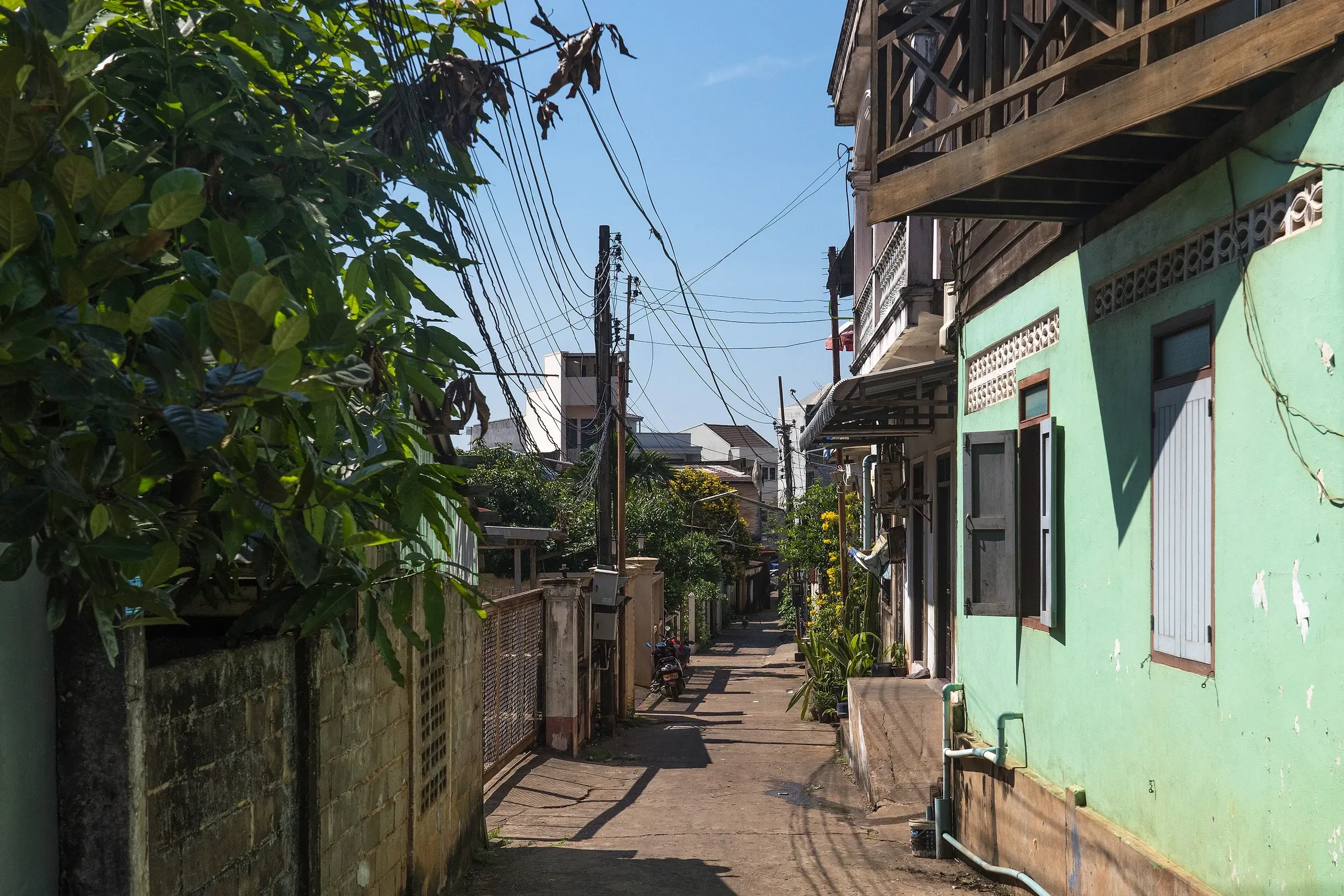 A quiet side street with houses and a mint green wall in Pakse