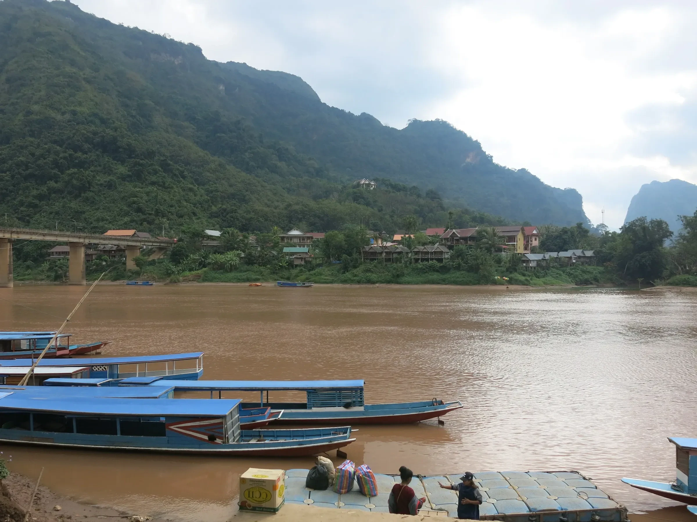 Long boats at the jetty in Nong Khiaw with forested karst hills behind