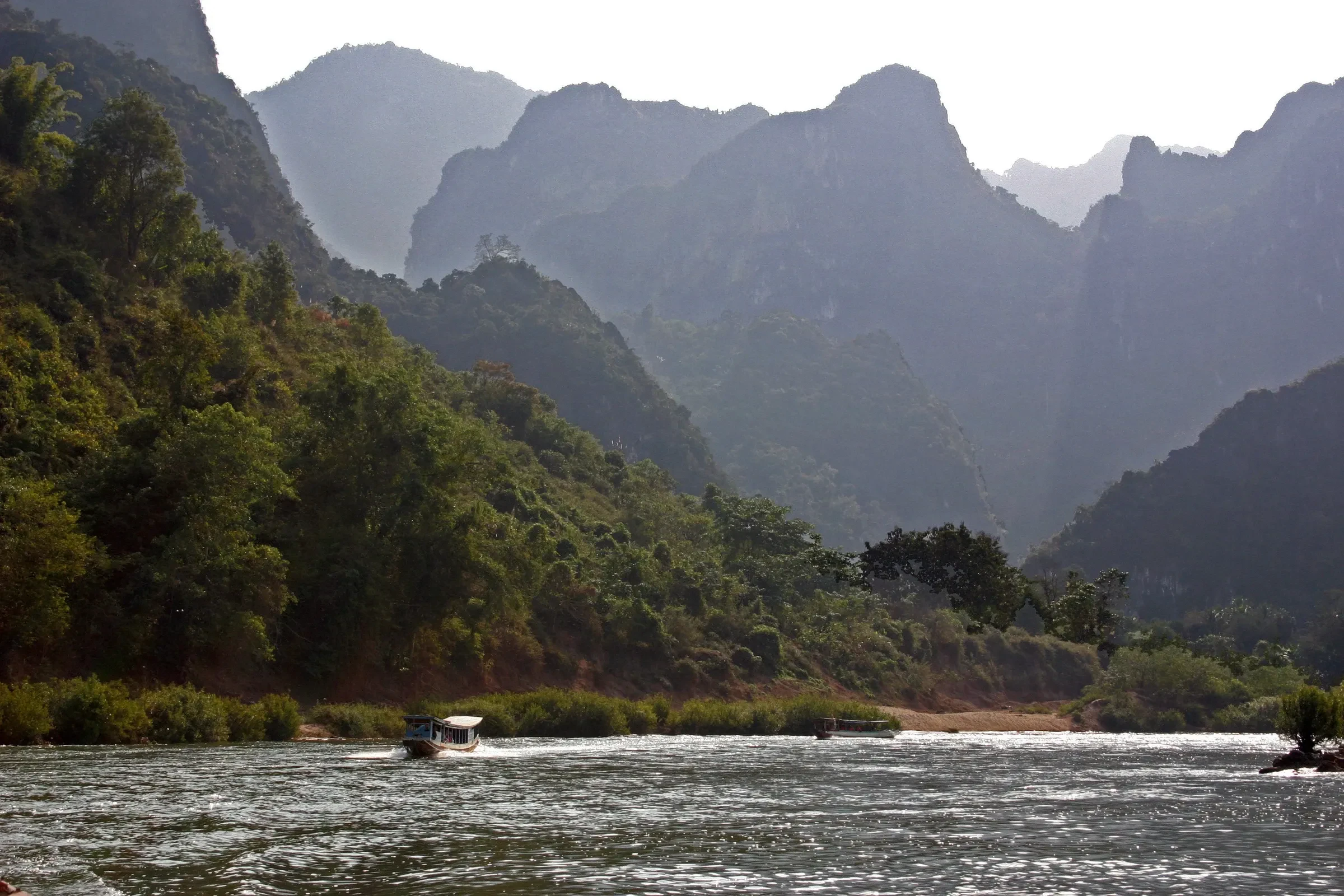 A boat on the Nam Ou river between steep forested karst hills