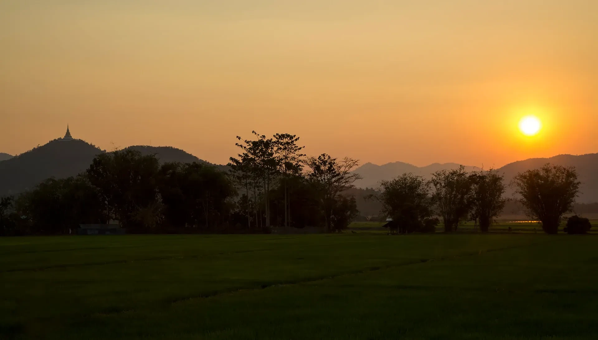 The sun setting behind fields and hills at Mae Sariang