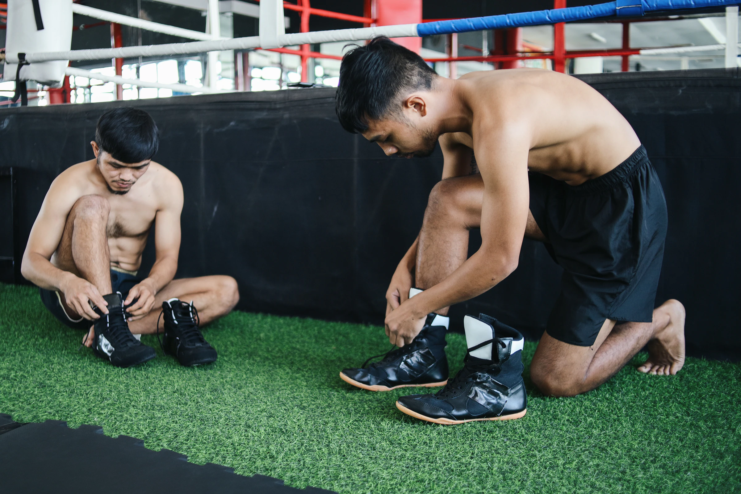 Two trainees lacing up their shoes beside a boxing ring