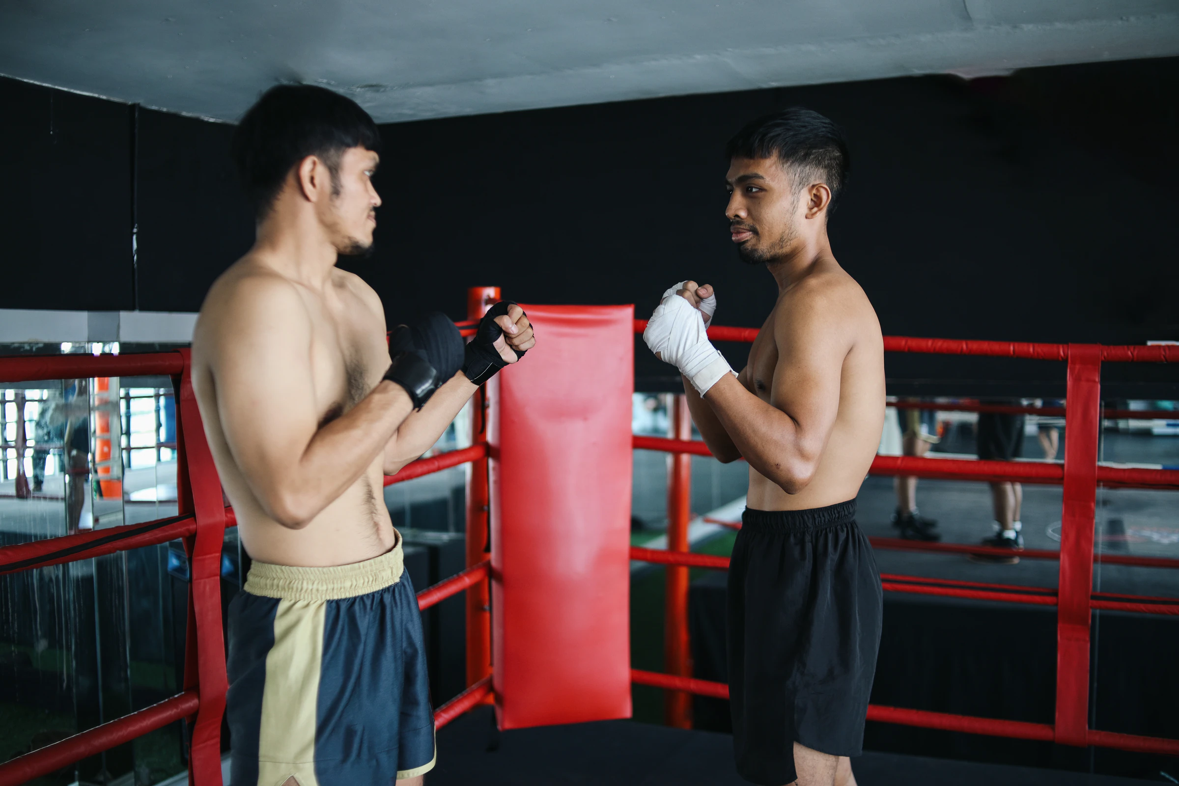 Two trainees in hand wraps standing ready beside a boxing ring