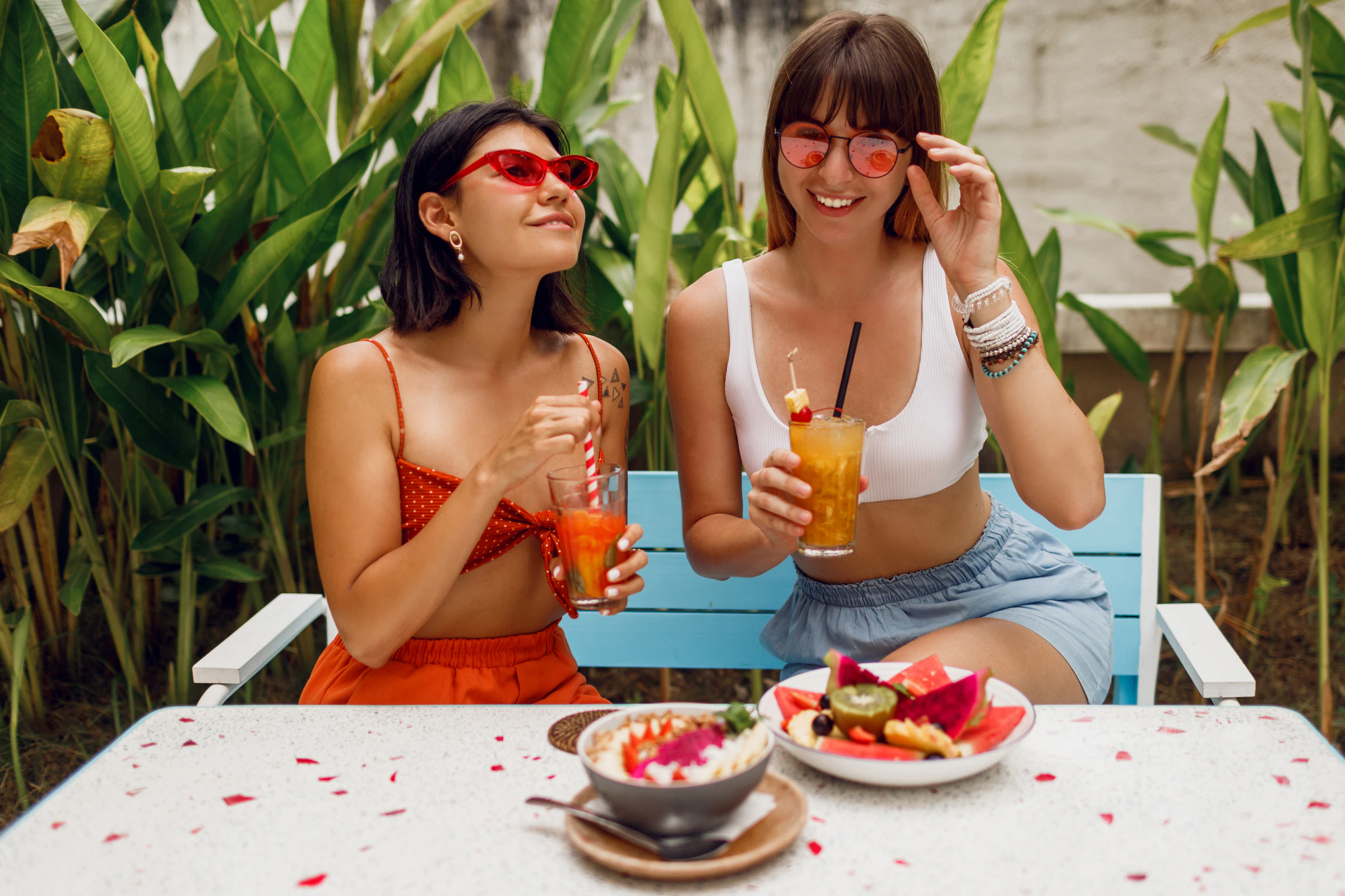 Two friends with fresh juices and a fruit bowl at a café table