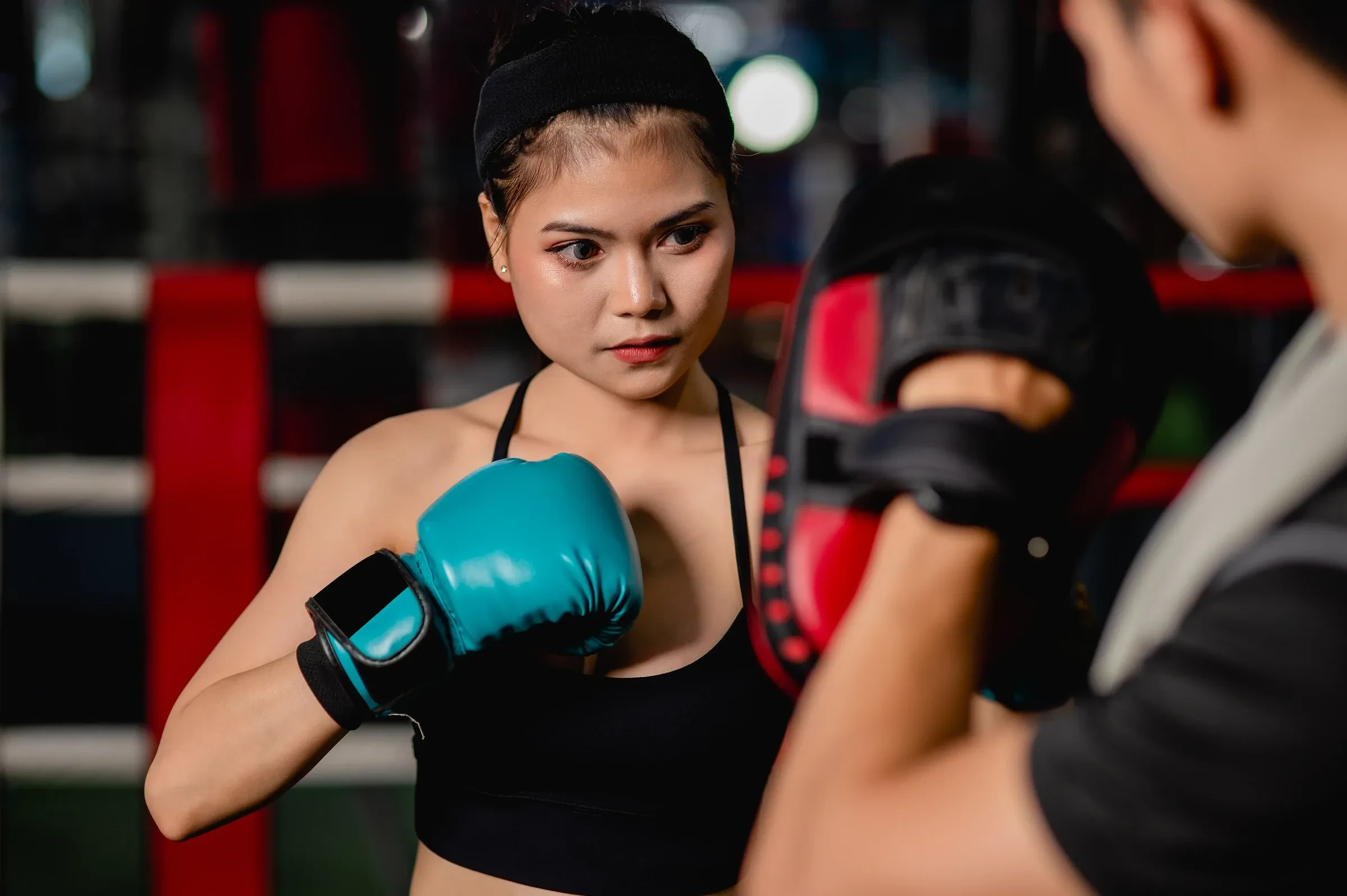 A trainee in teal gloves working combinations on a trainer's mitts