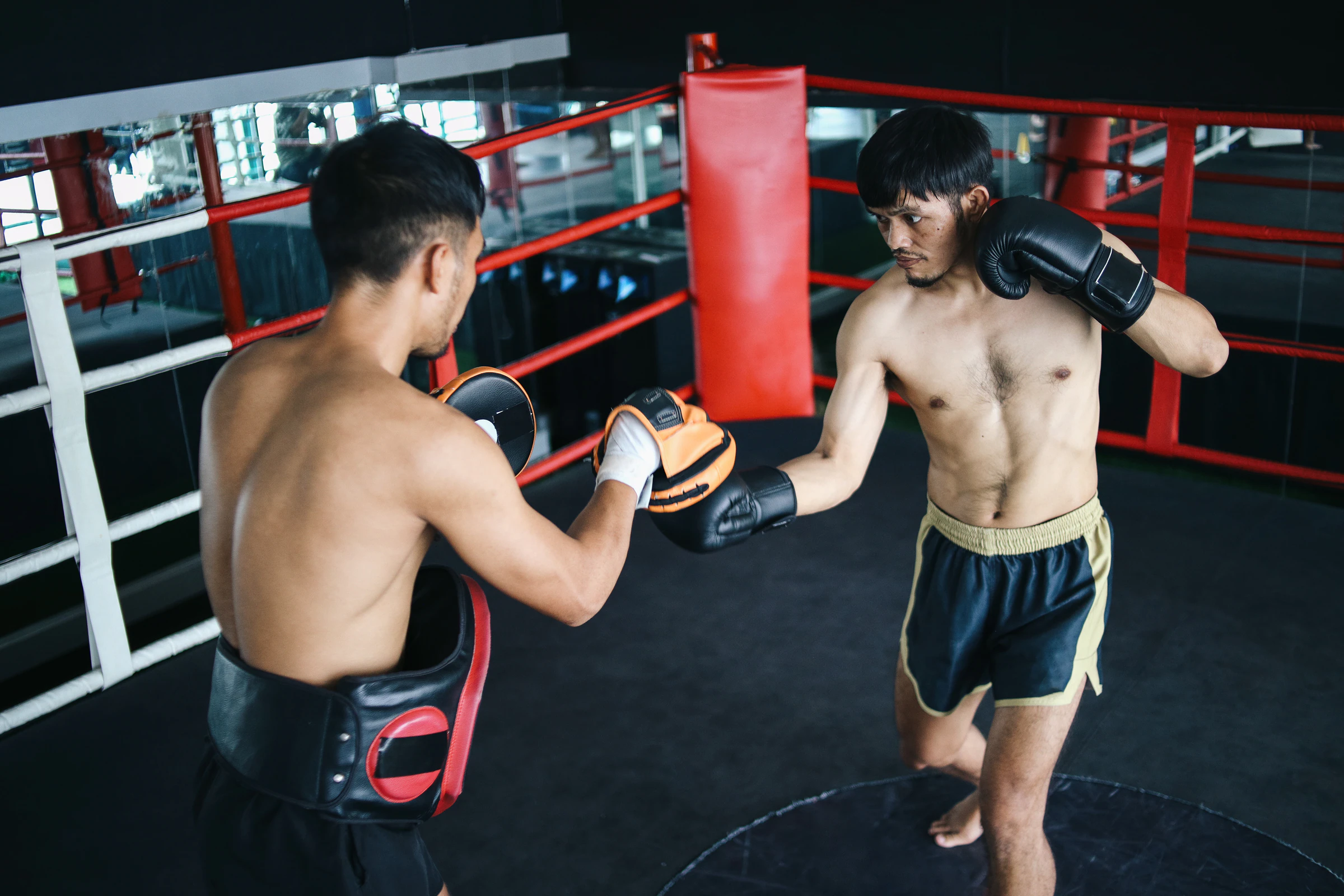 A trainee and a trainer working pads inside a boxing ring