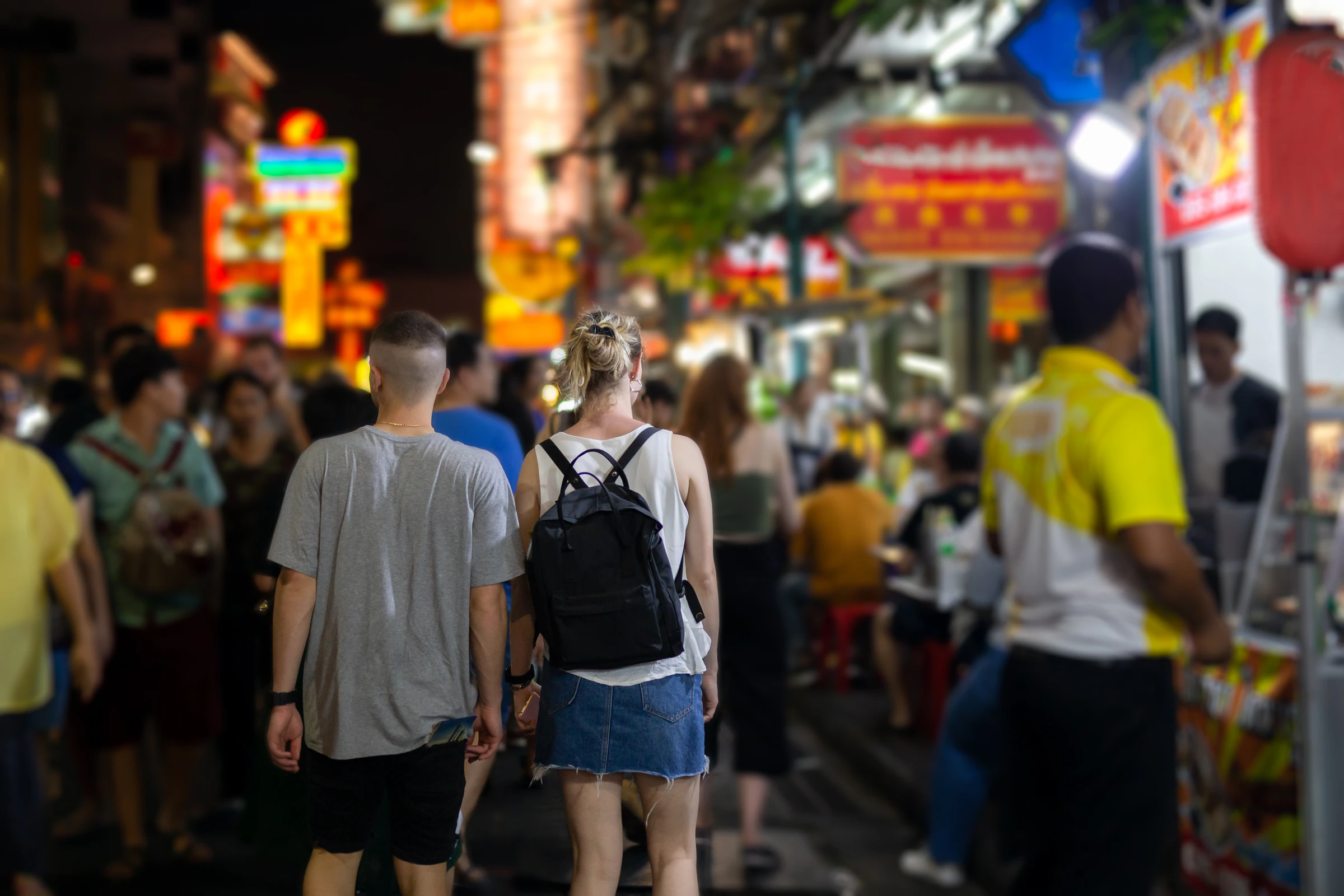 Travellers walking along a crowded Bangkok street lit up at night
