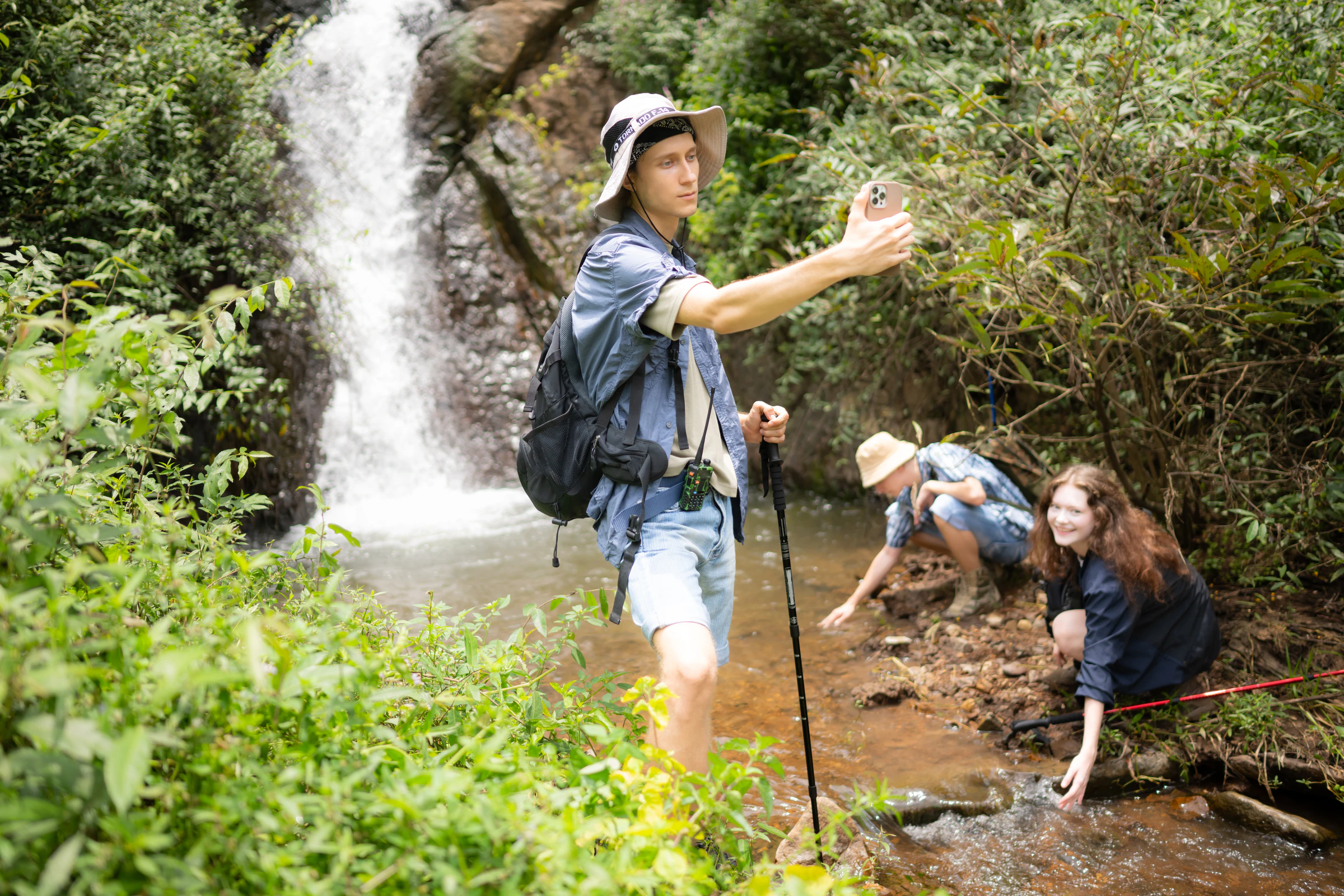 Hikers with walking poles beside a small waterfall in the forest