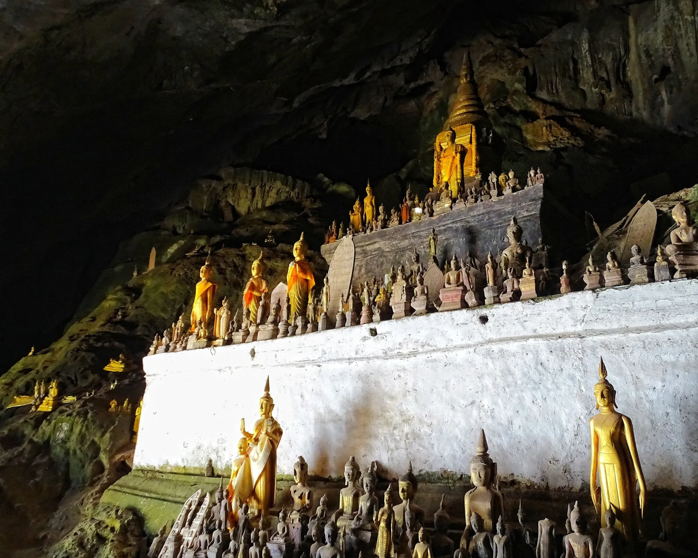 Gilded Buddha statues on a white ledge inside a Pak Ou cave above the Mekong