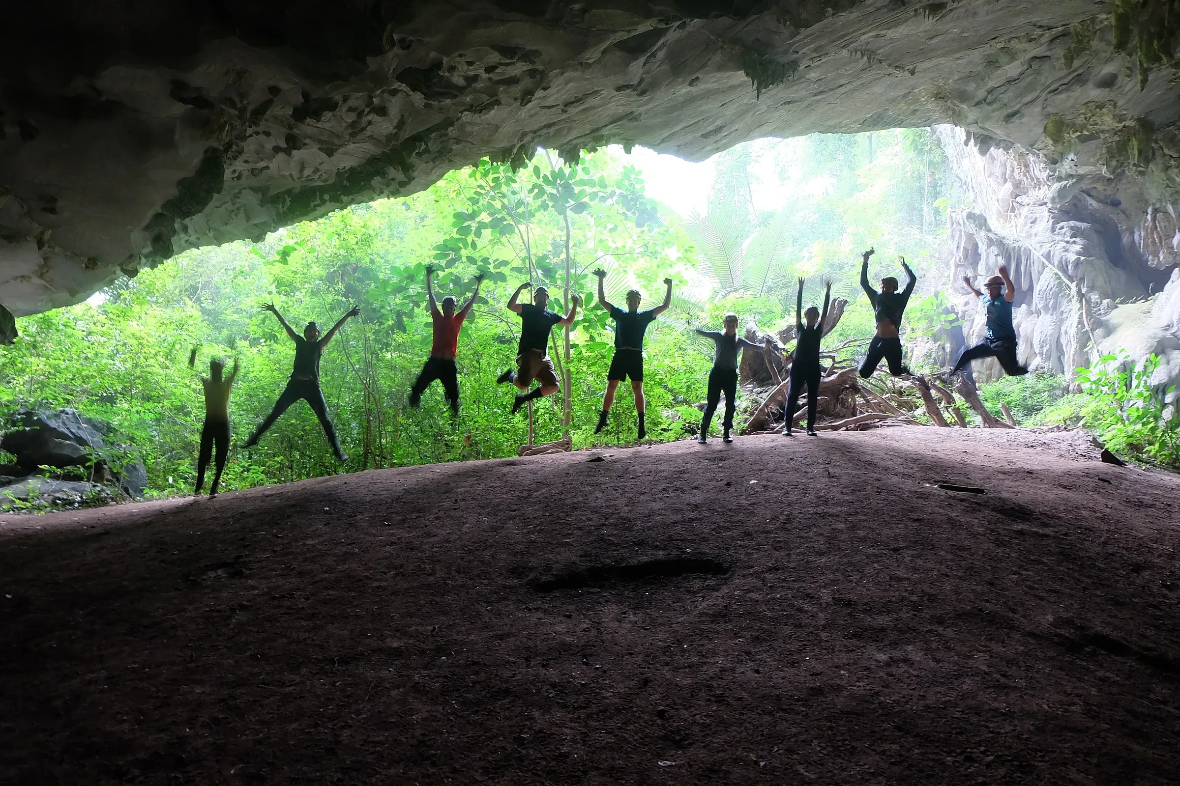 A group of trekkers in silhouette at a jungle cave mouth in Phong Nha-Ke Bang