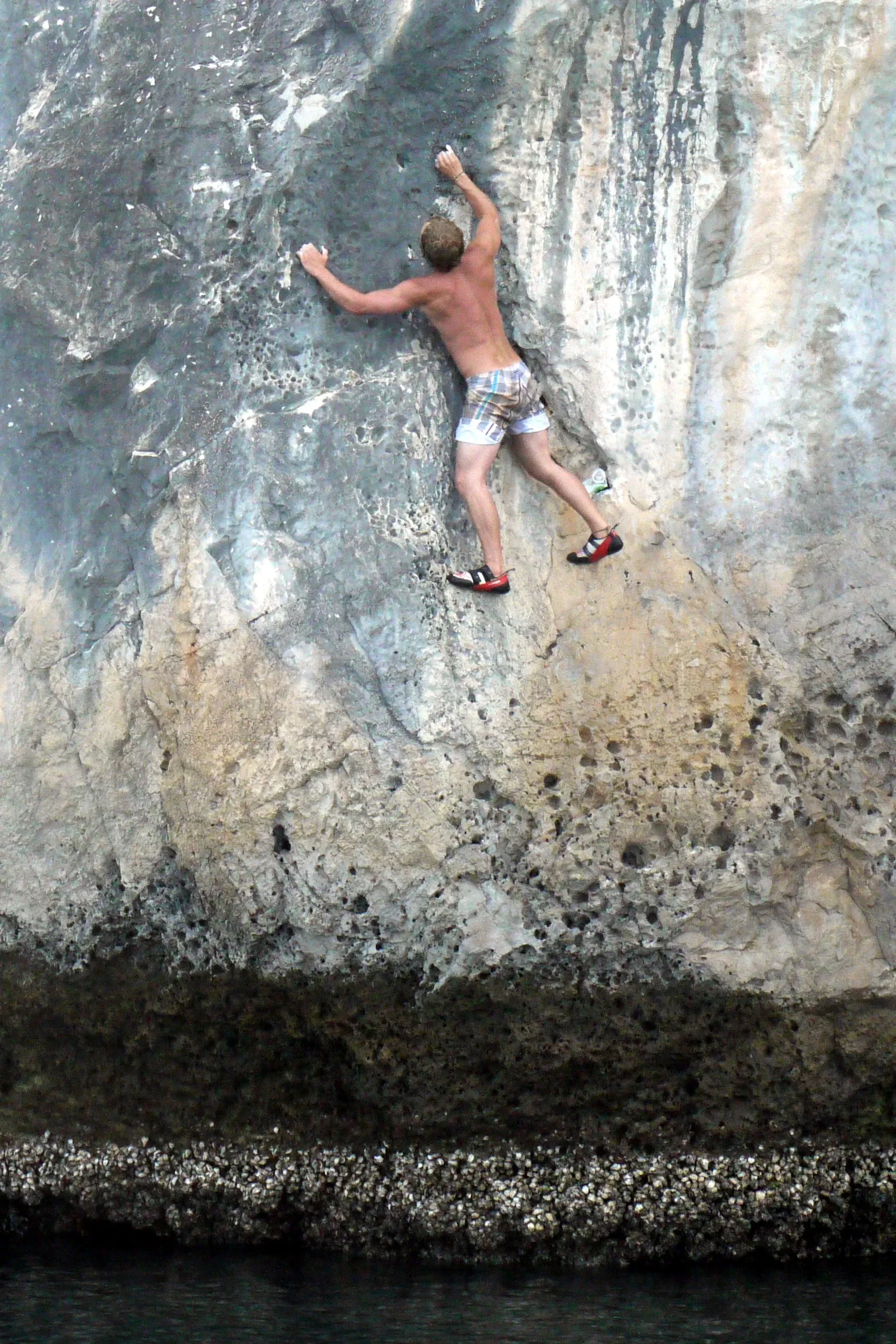 A climber deep water soloing on a sea cliff near Tonsai