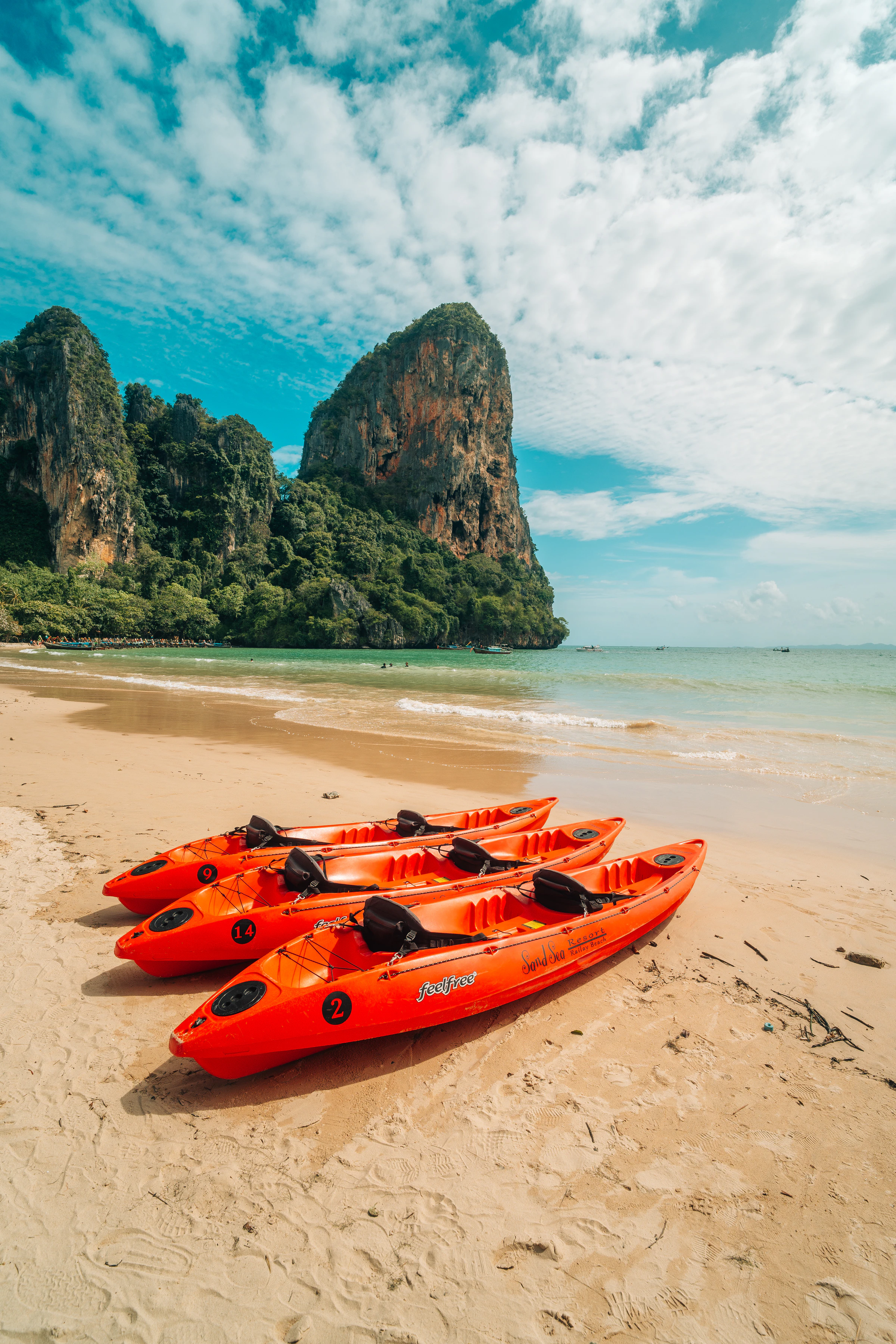Orange rental kayaks on Railay beach below a limestone tower