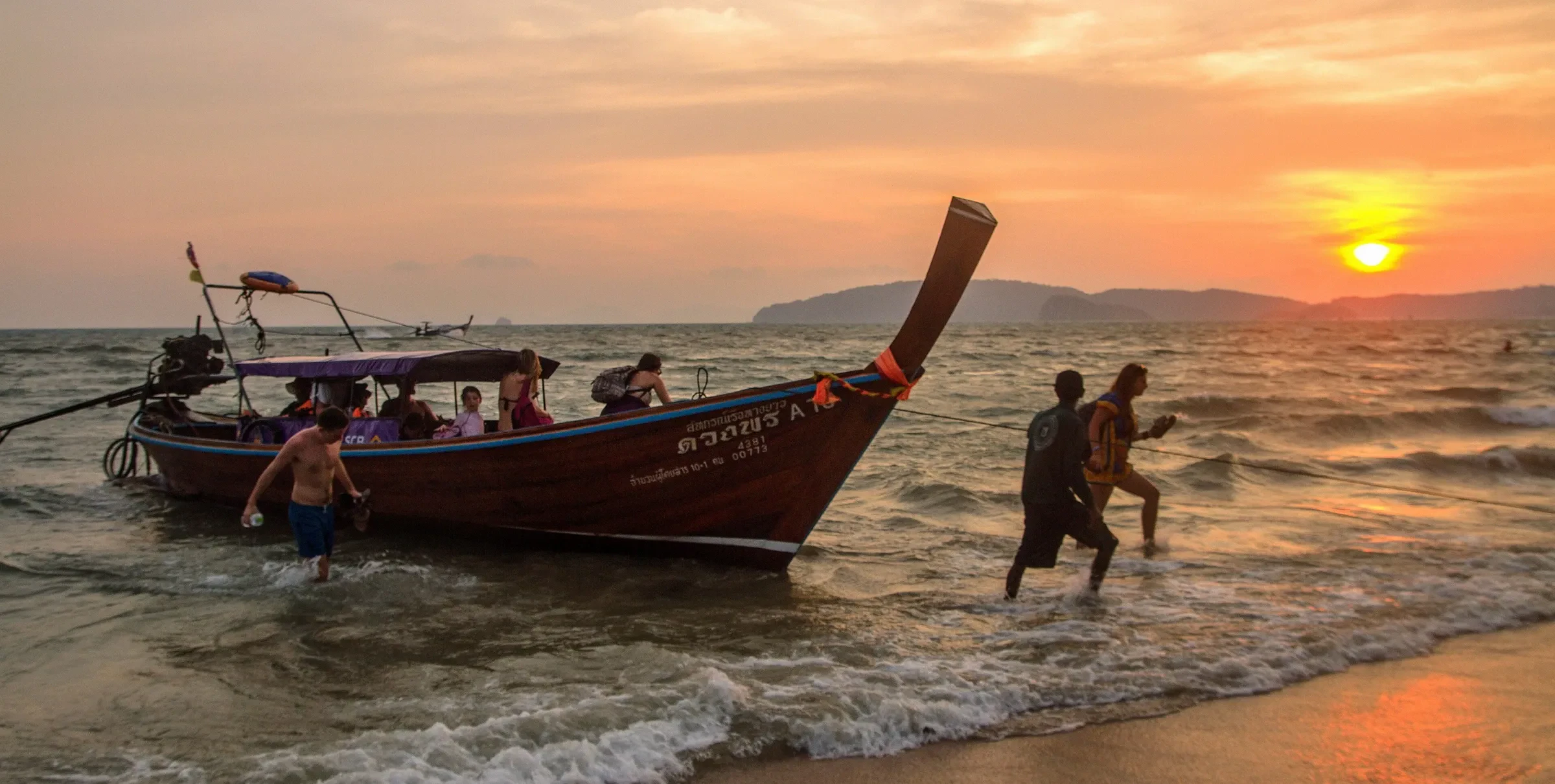 A longtail boat landing on Ao Nang beach at sunset