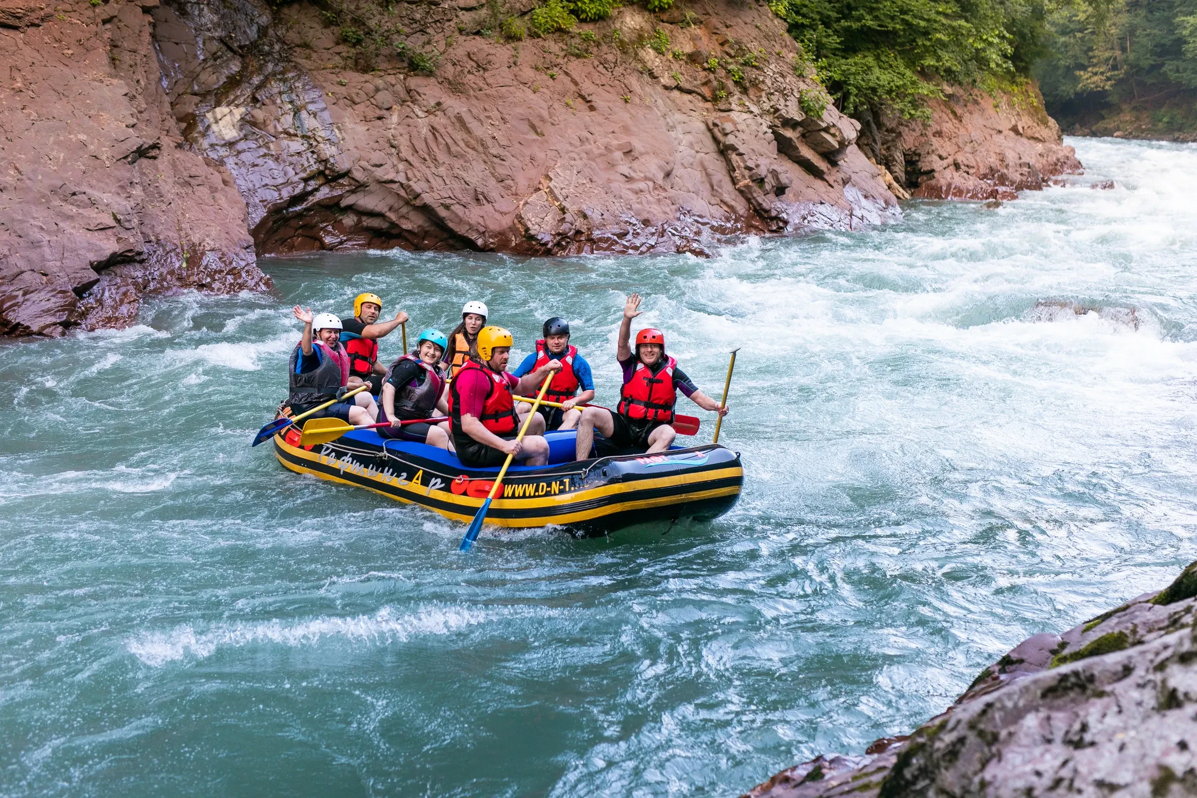 A raft crew in helmets and life jackets paddling through rapids