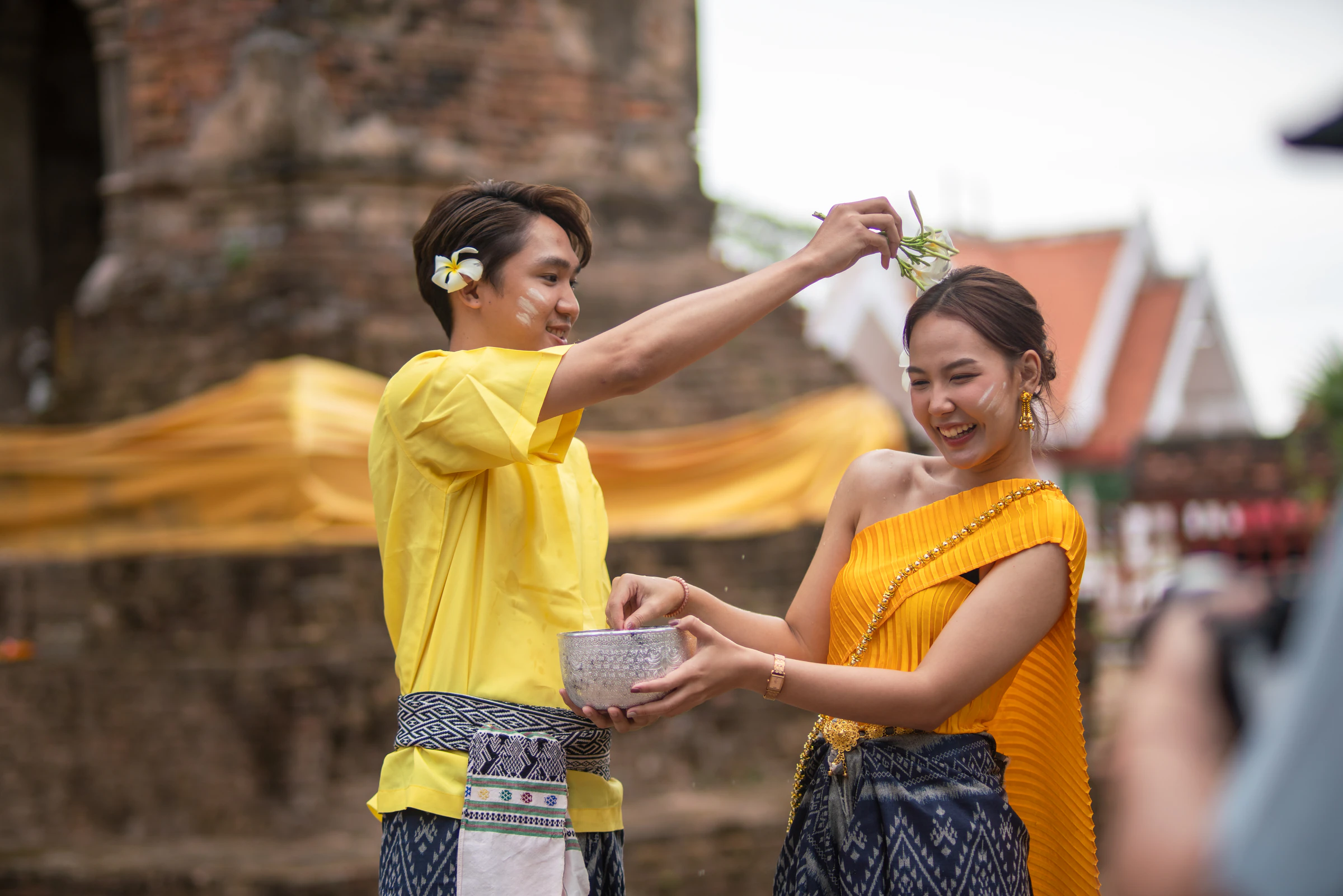 A young couple in Thai dress splashing water at a temple during Songkran